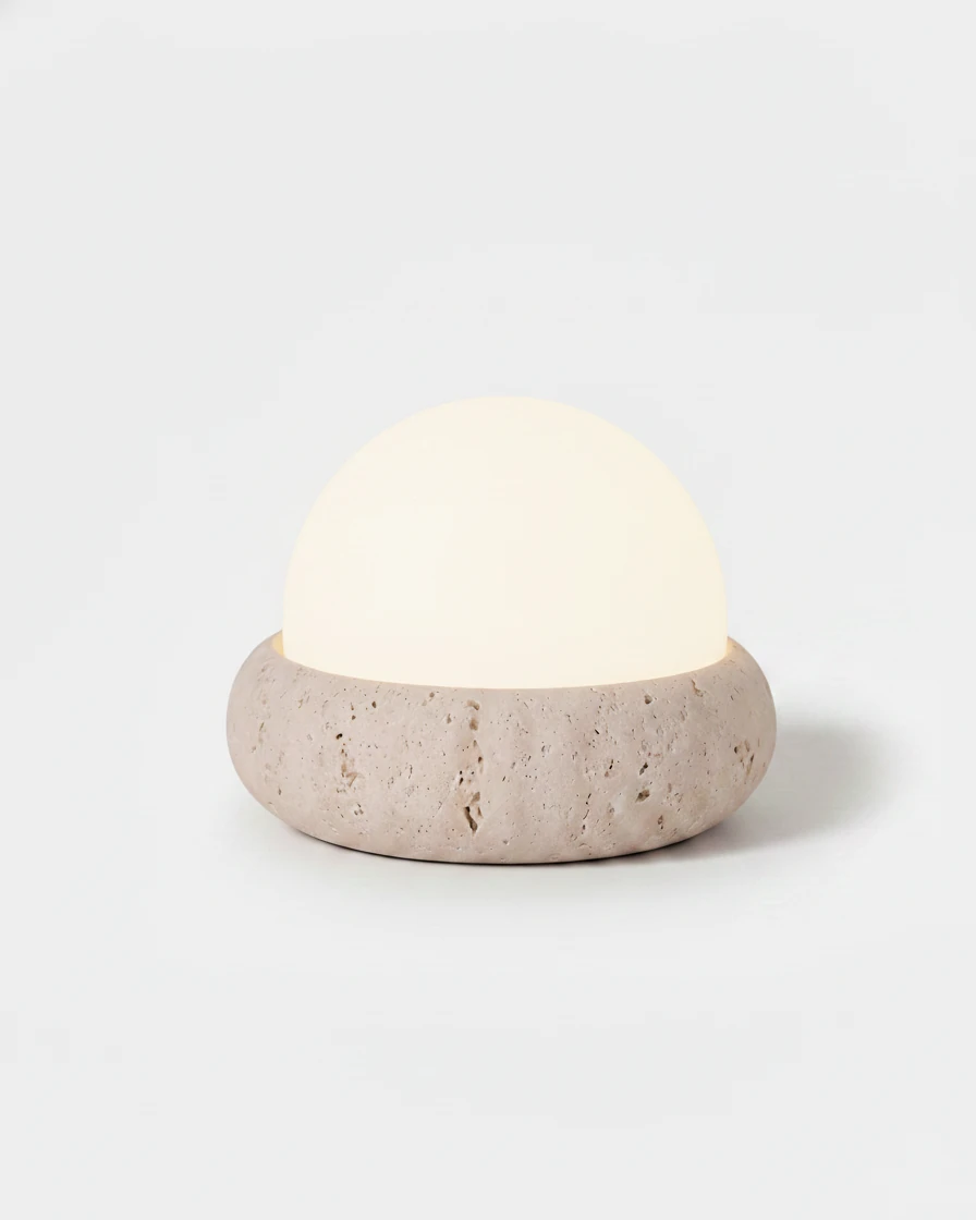 Cordless outdoor table lamp LUCE No.01, opal glass dome switched on over a rounded travertine base