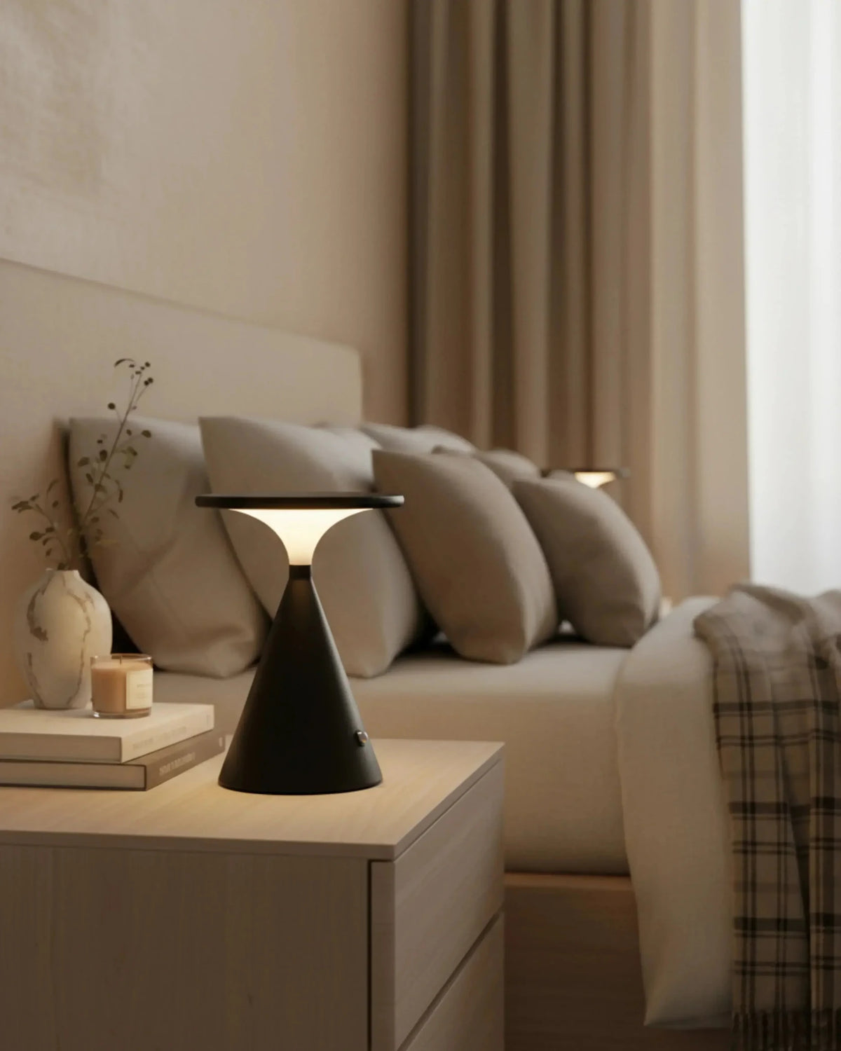 Cordless table lamp SOSTA No.01 in matte black lit on a nightstand beside a bed with neutral bedding