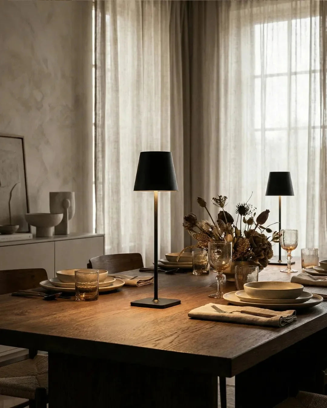 Cordless table lamp FOGGIA No.01, two black cone-shade lamps lit on a dark wood dining table set for dinner