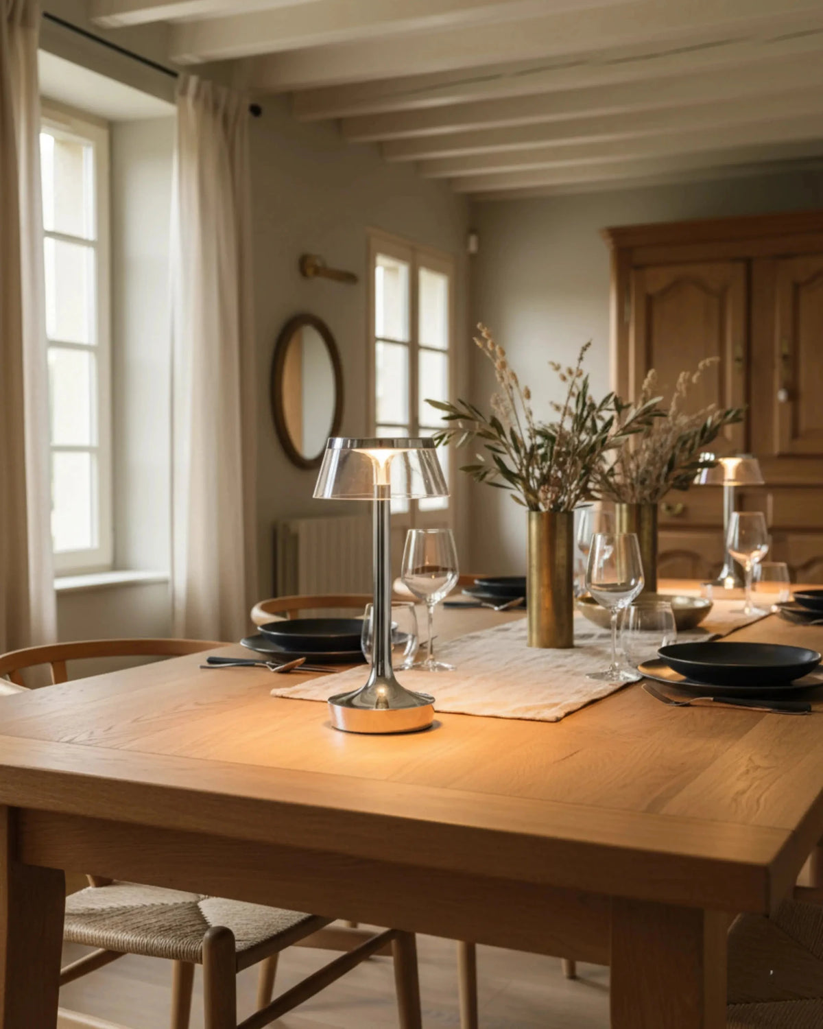 Cordless table lamp ZARA No.01 in polished chrome lit on a wooden dining table set with glasses and plates