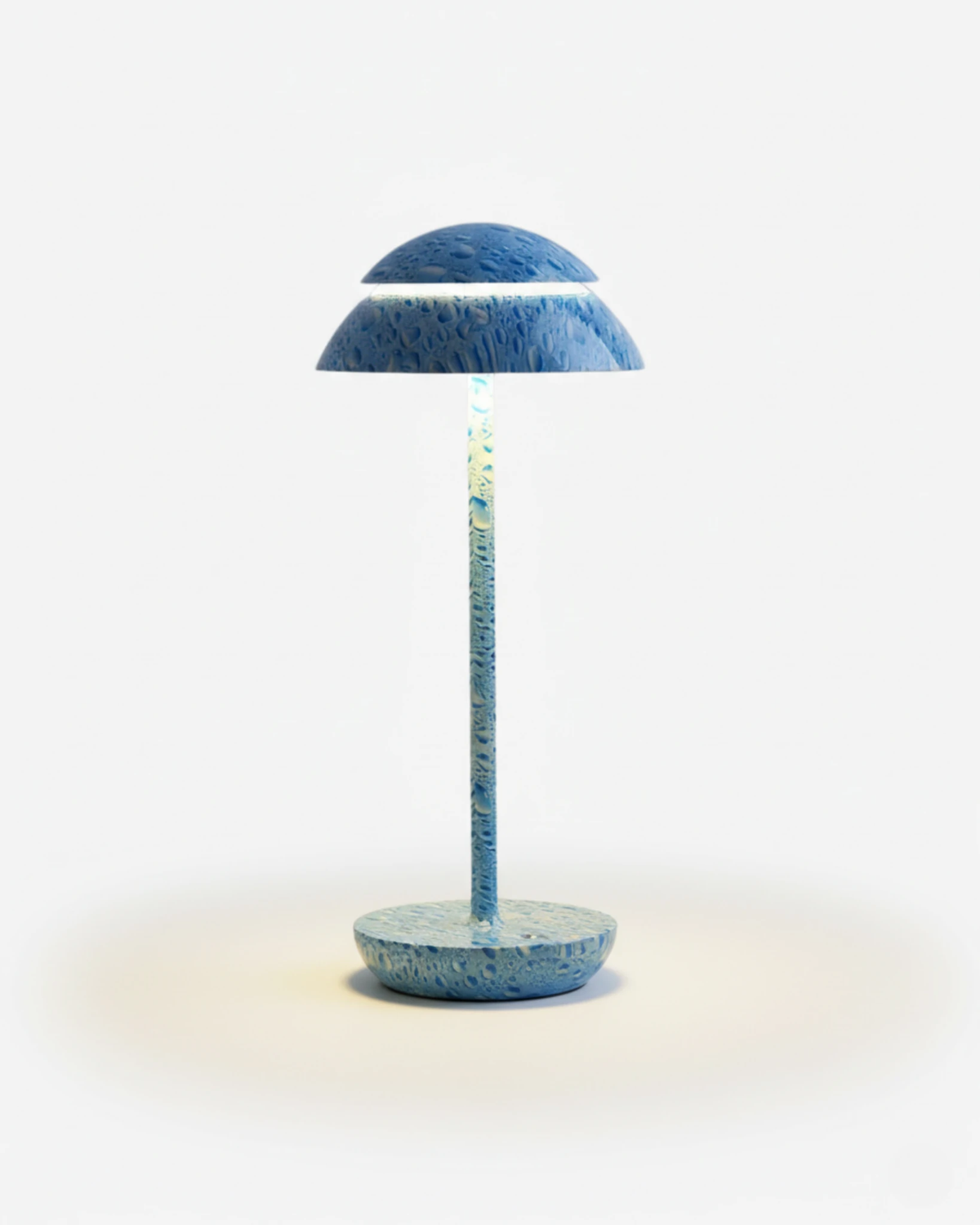 Cordless table lamp CALMA No.01 with a blue speckled dome cap, stem and disc base, switched on