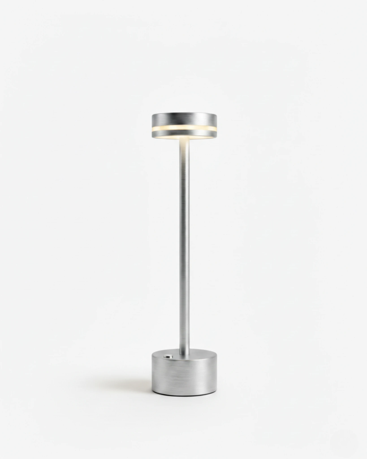Cordless table lamp NIDO No.02 in Silver, thin aluminum stem topped by a glowing disc on a plain background
