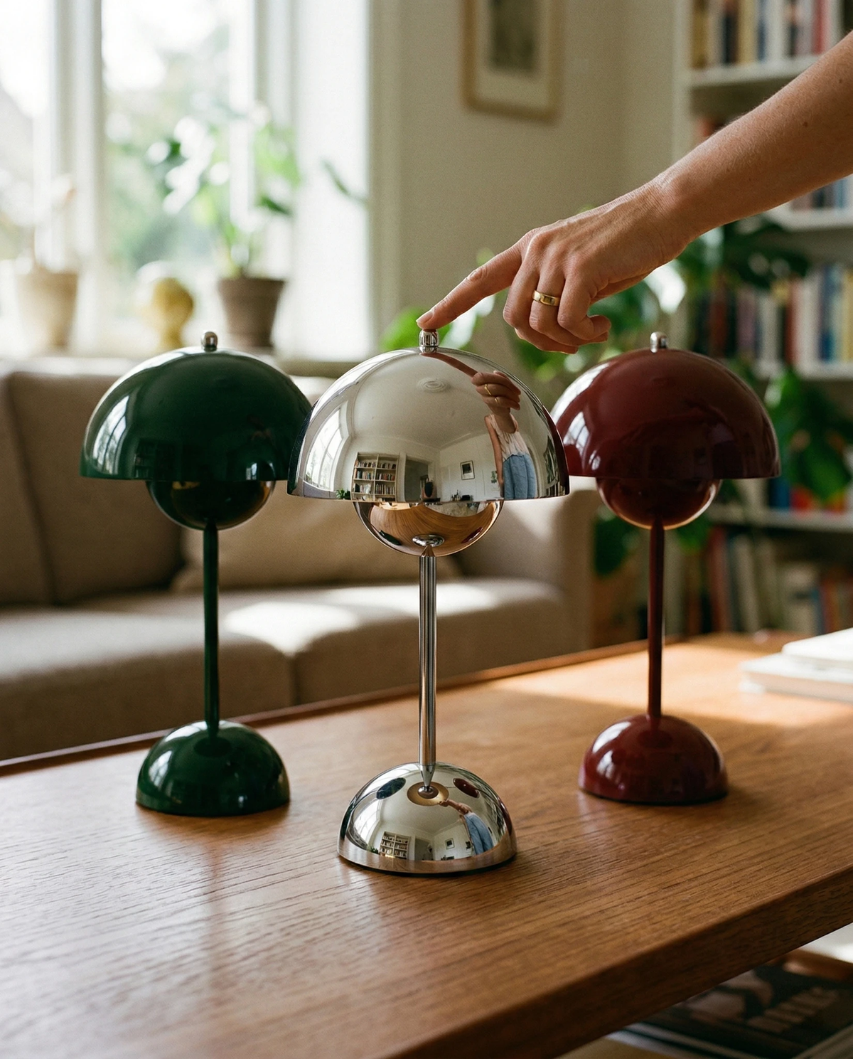 Three cordless table lamps DOMA No.02 in green, chrome and wine red on a wooden table, a hand touching the chrome dome
