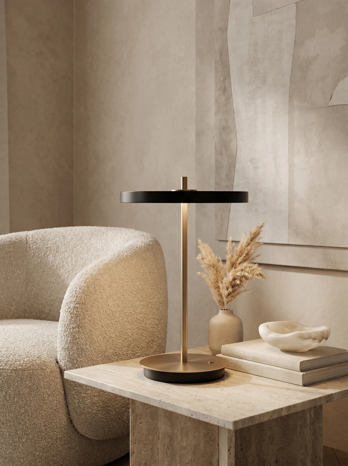 Cordless table lamp SALA No.01 in matte black, switched on atop a travertine cube table next to a boucle armchair