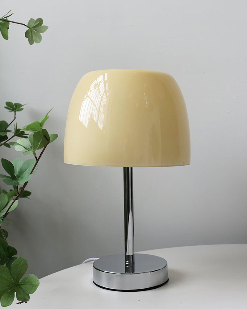 Glass table lamp VENEZIA No.01 with beige shade on a white round table next to green foliage, unlit