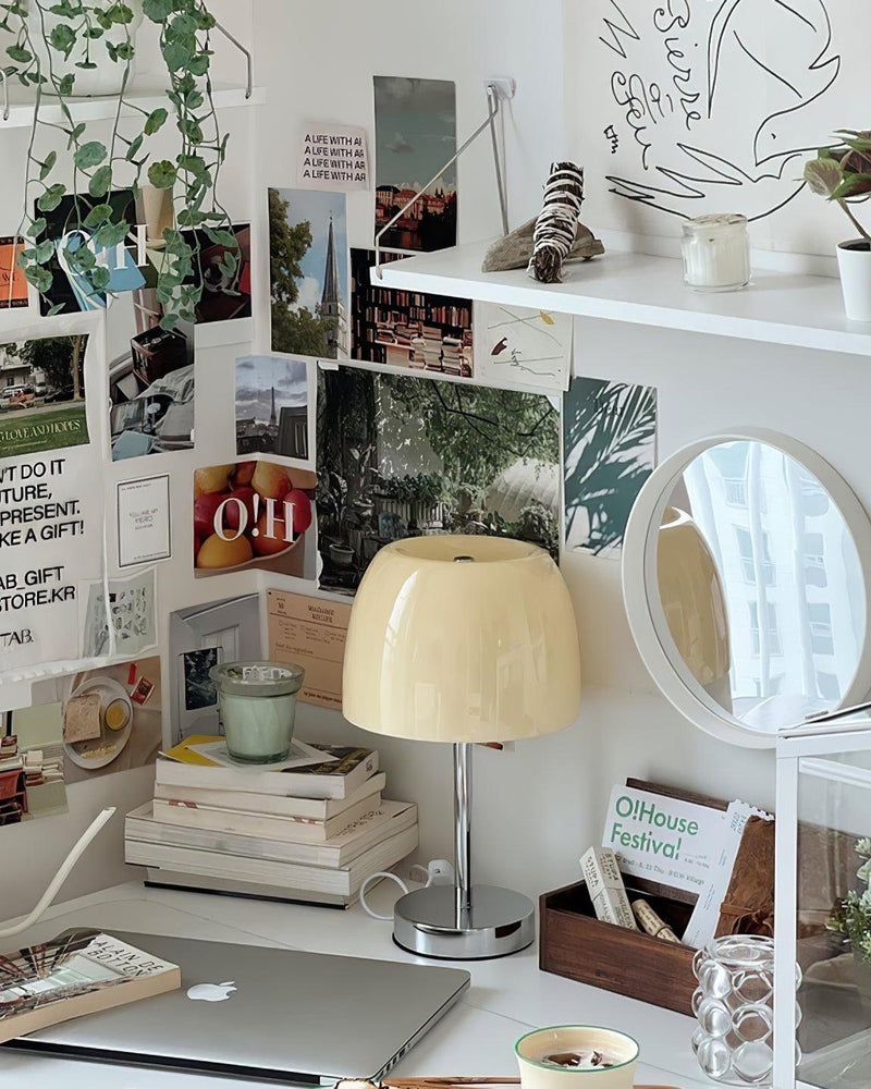 Glass table lamp VENEZIA No.01 with cream shade on a desk beneath a wall of pinned photos and prints, unlit