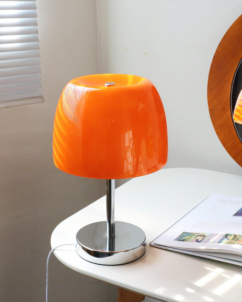 Glass table lamp VENEZIA No.01 with orange shade, unlit, on a white table with magazines beside a round mirror