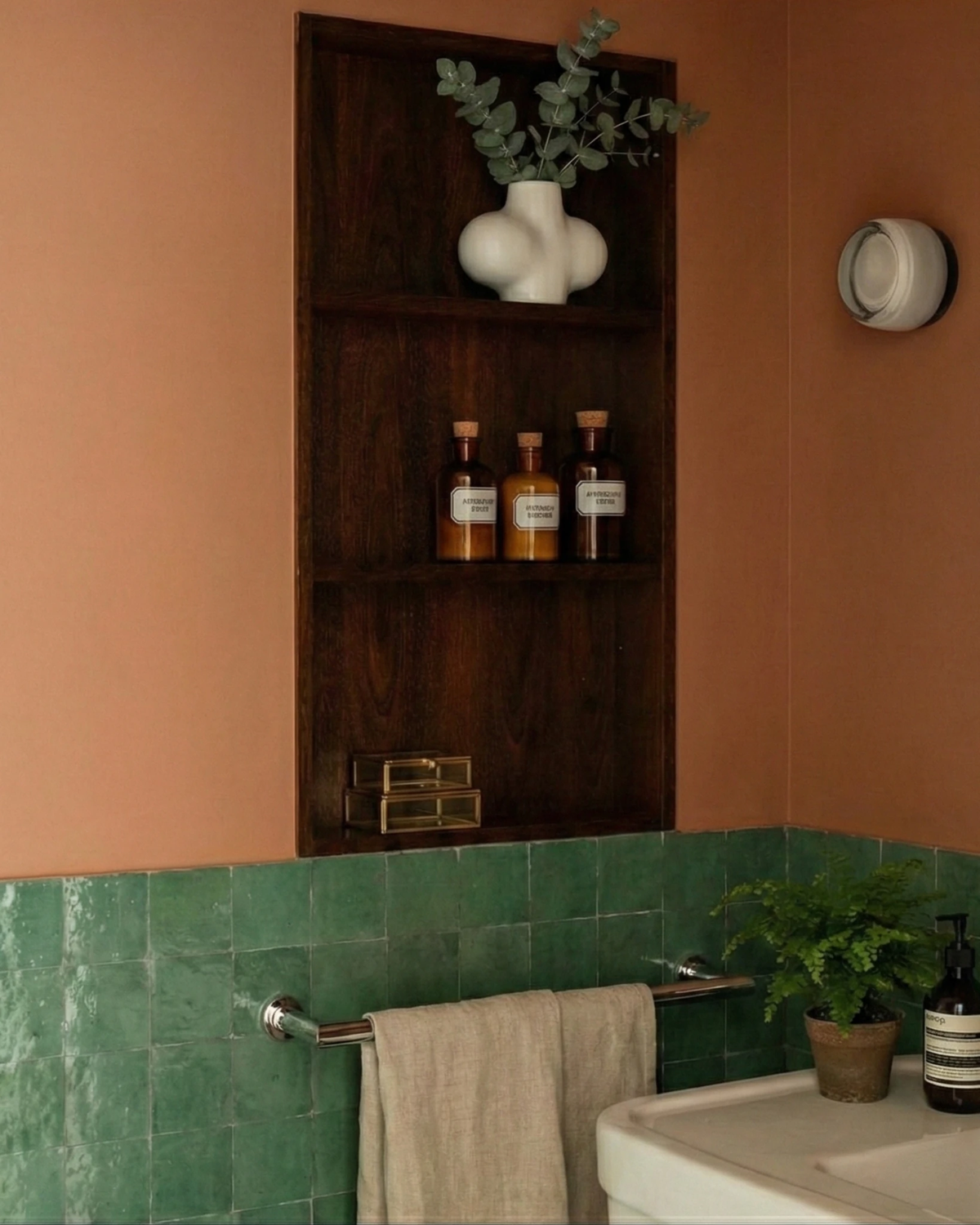 Glass wall sconce HALO No.08 in opal glass on a terracotta bathroom wall next to a wooden shelf niche