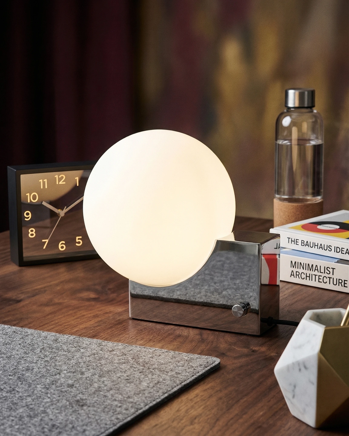 Globe desk lamp NOVA No.01 in chrome lit on a walnut desk with a felt mat, retro clock and books