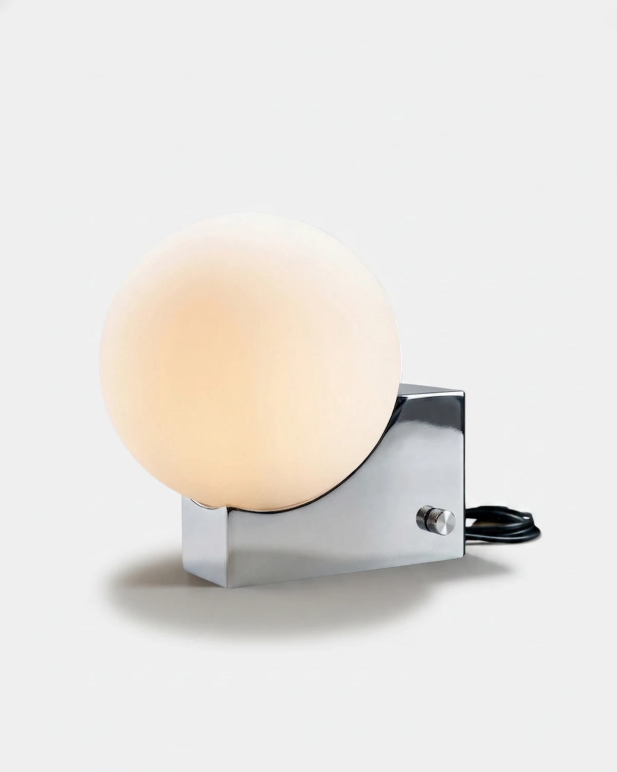 Globe desk lamp NOVA No.01 in Polished Chrome, opal globe resting on a mirrored block base, softly glowing