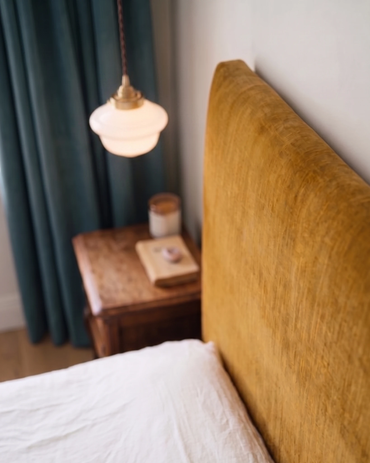 Globe pendant light SCOLA No.01 switched on over a nightstand next to a mustard velvet headboard