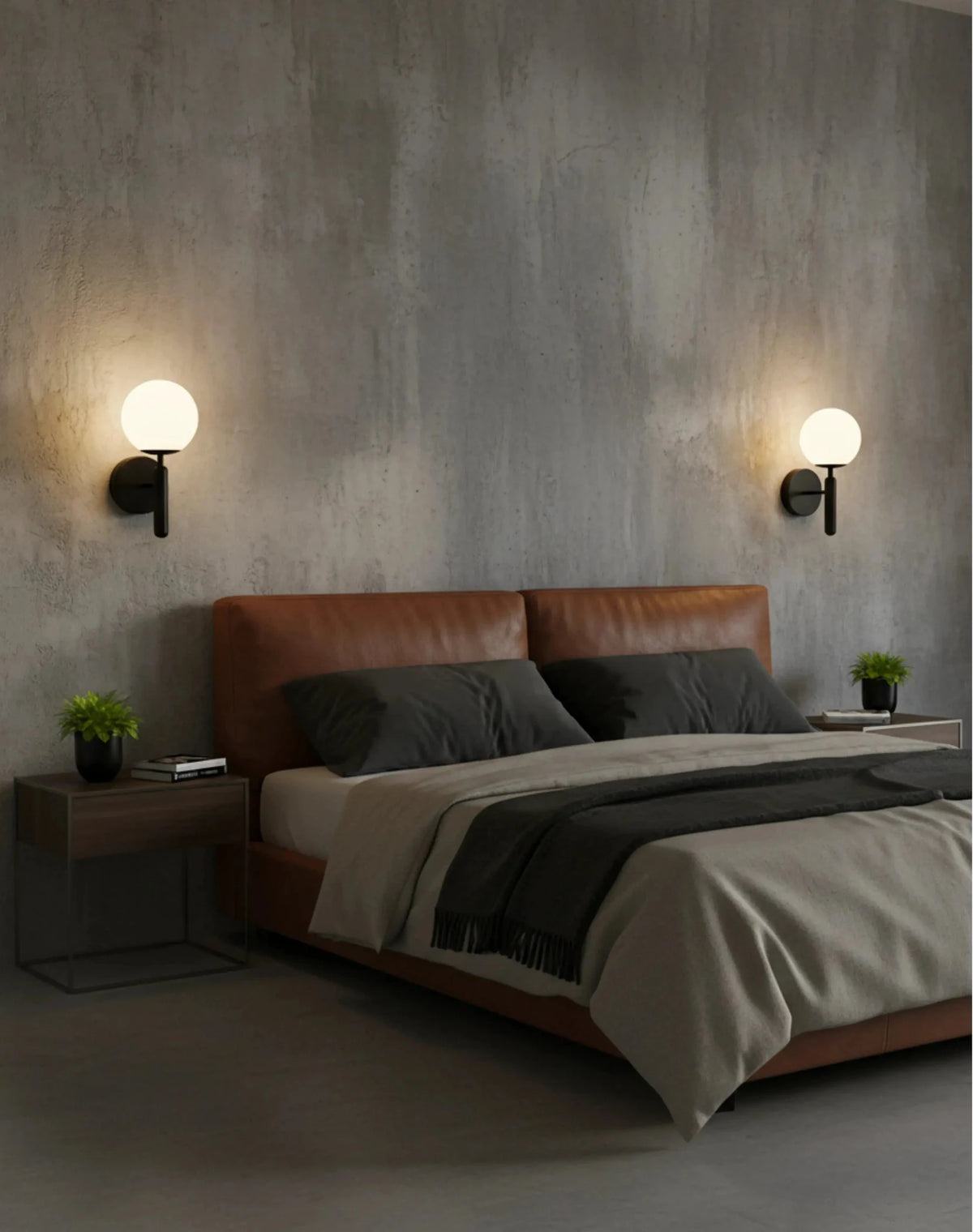 Pair of globe wall sconces CIELO No.01 in matte black lit above a tan leather bed against a concrete wall