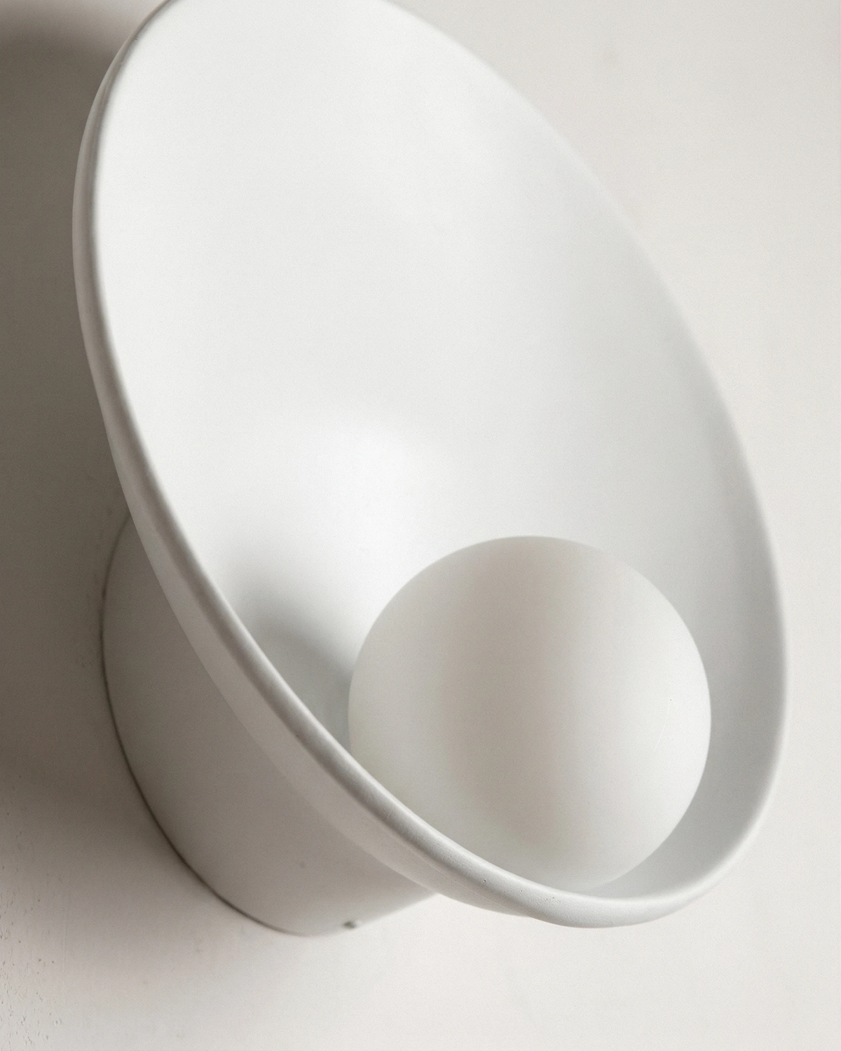 Close-up of the white resin shell and opal glass globe of the OASI No.01 globe wall sconce, unlit