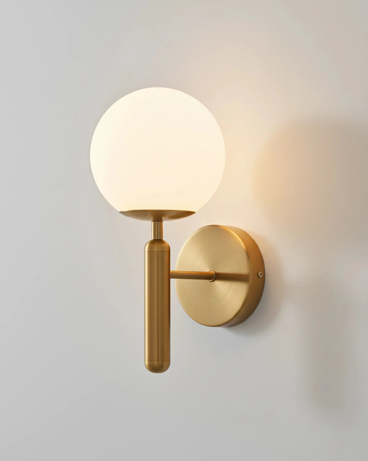 Globe wall sconce CIELO No.01 in brushed brass, opal globe switched on above a brass arm and backplate