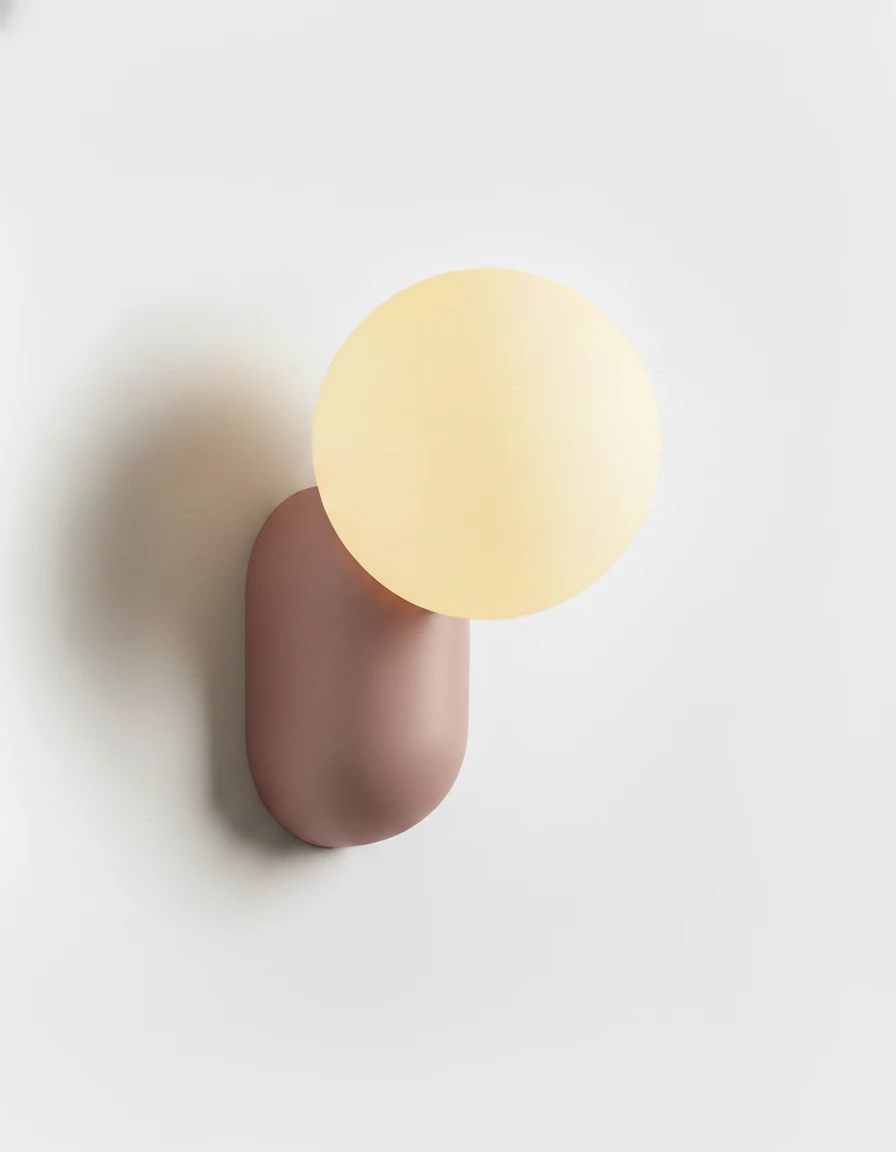 Globe wall sconce AURA No.04 in Powder Pink, dusty pink resin capsule with a lit opal glass globe