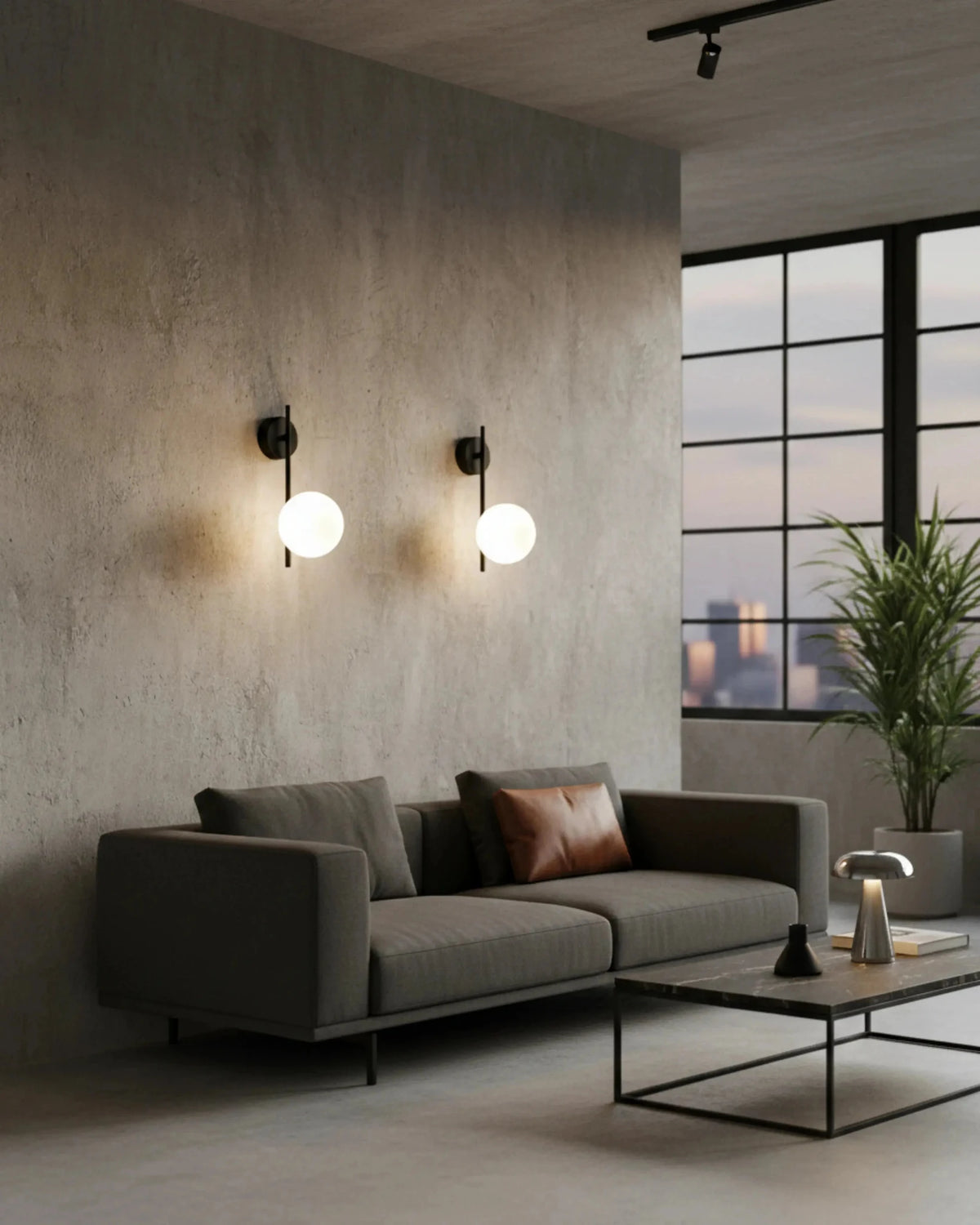 Two globe wall sconces ASTRO No.01 in matte black lit on a concrete wall above a gray sofa with a city view