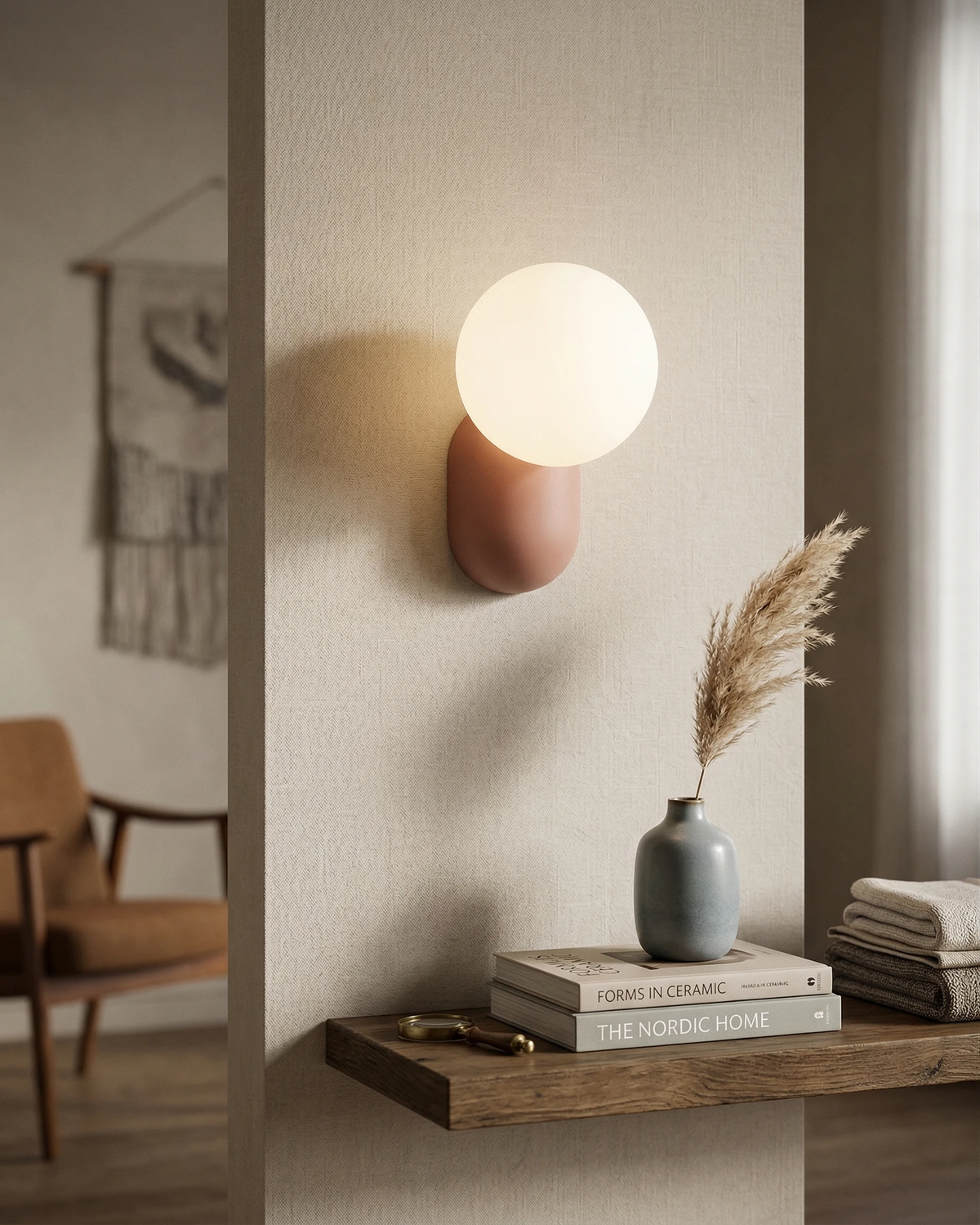Globe wall sconce AURA No.04 in powder pink switched on above a floating wood shelf with books and a vase