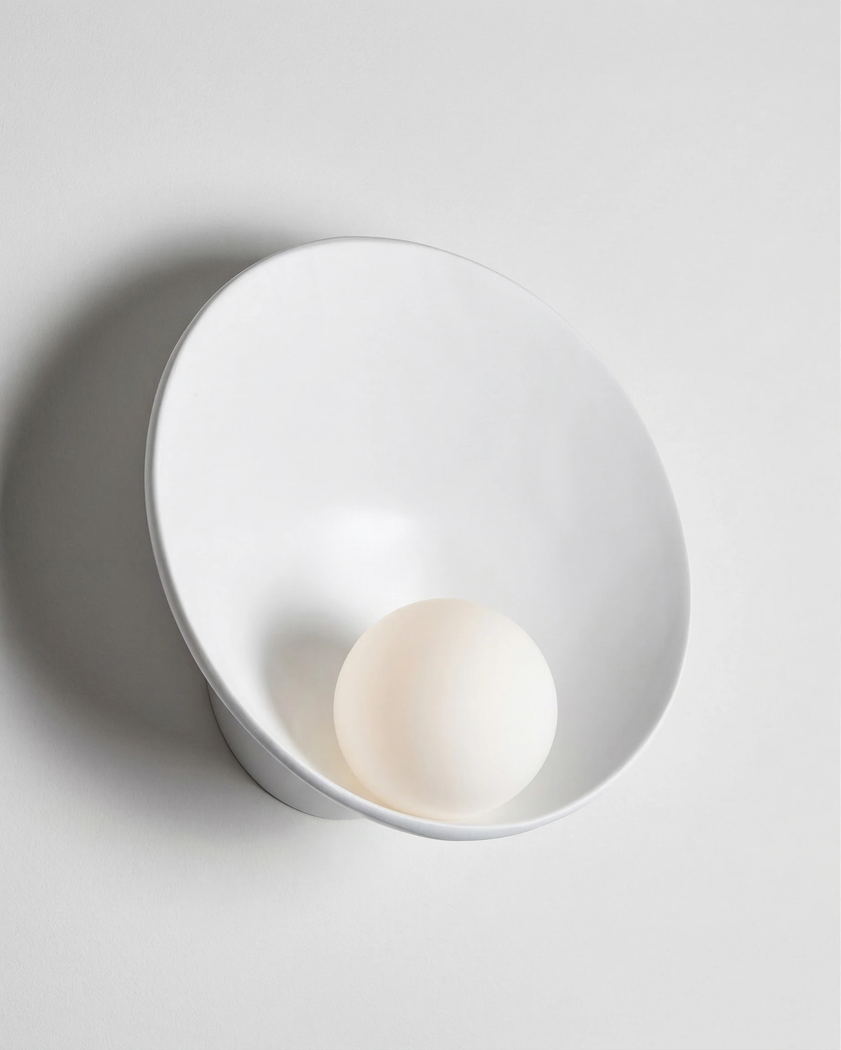 Globe wall sconce OASI No.01 in pure white, curved resin shell holding an opal glass globe, unlit