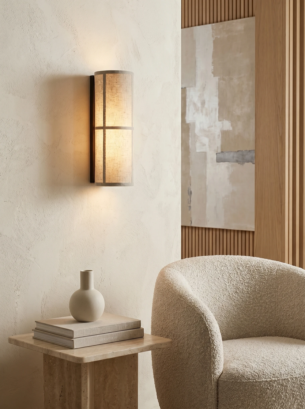 Linen shade wall sconce FUMO No.01 switched on next to a painting above a side table and boucle armchair