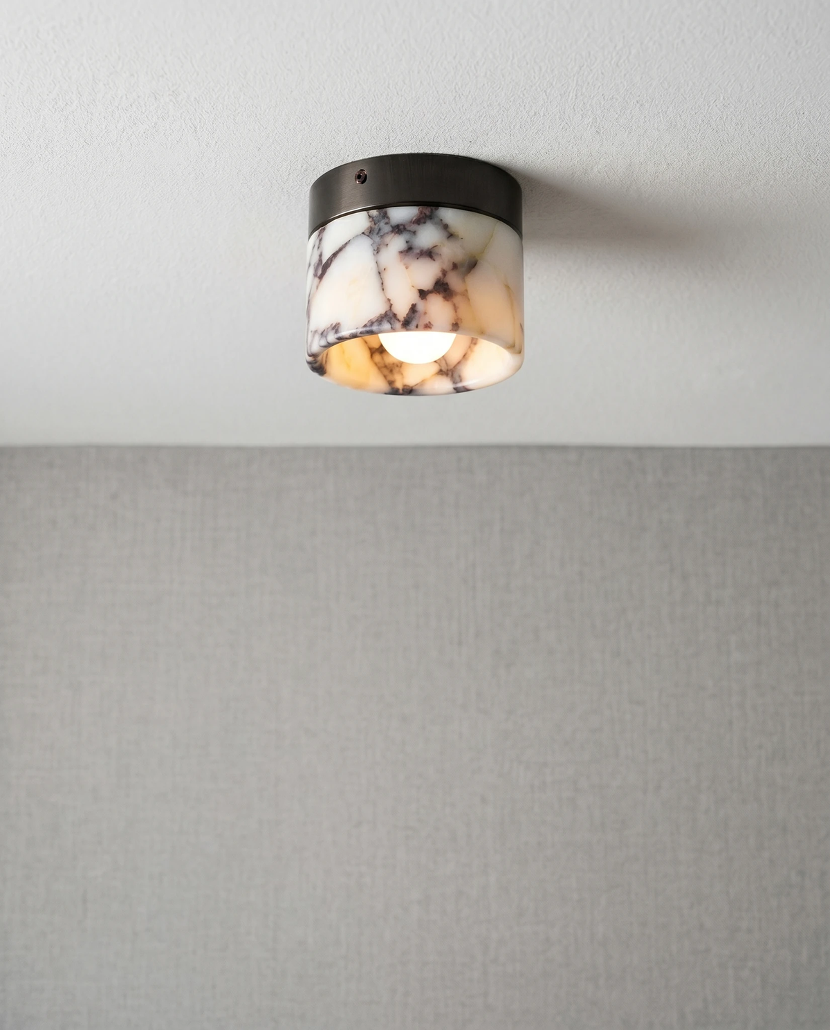 Marble flush mount ceiling light NERA No.06 switched on in a ceiling corner above a plain gray wall