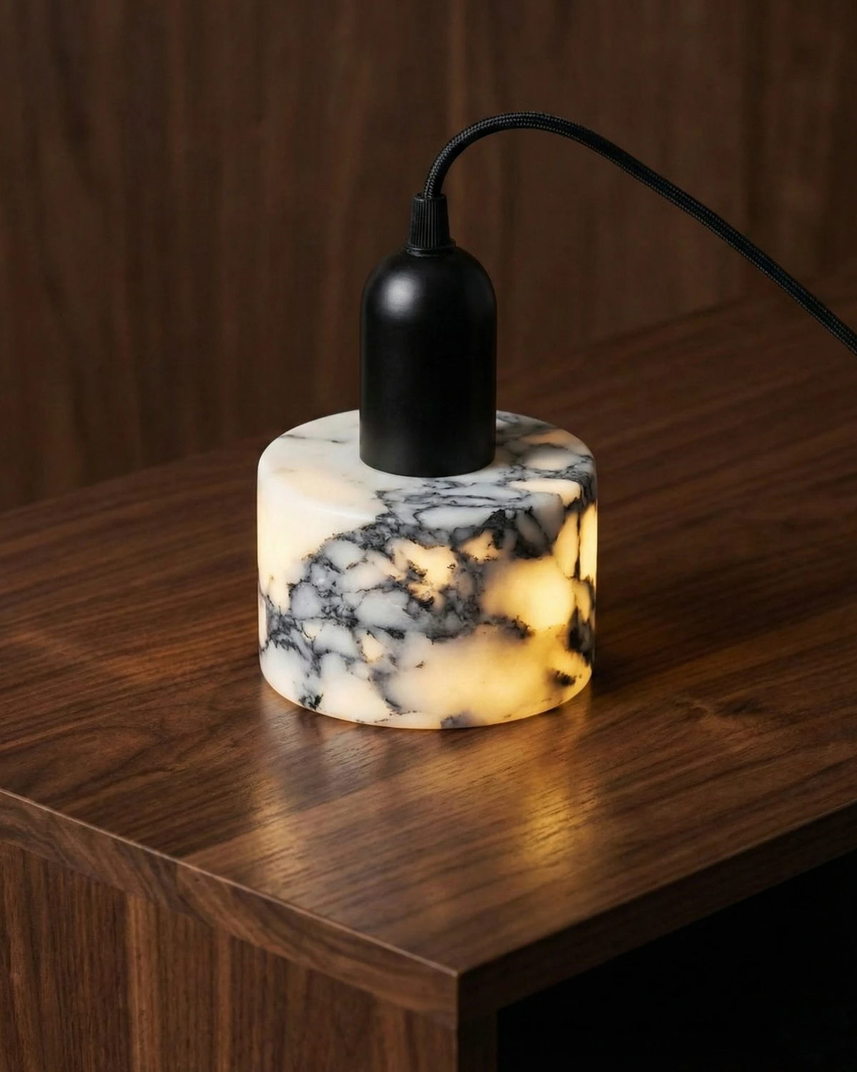 Marble pendant light MARMI No.02 resting lit on the edge of a walnut table, black socket and cord above