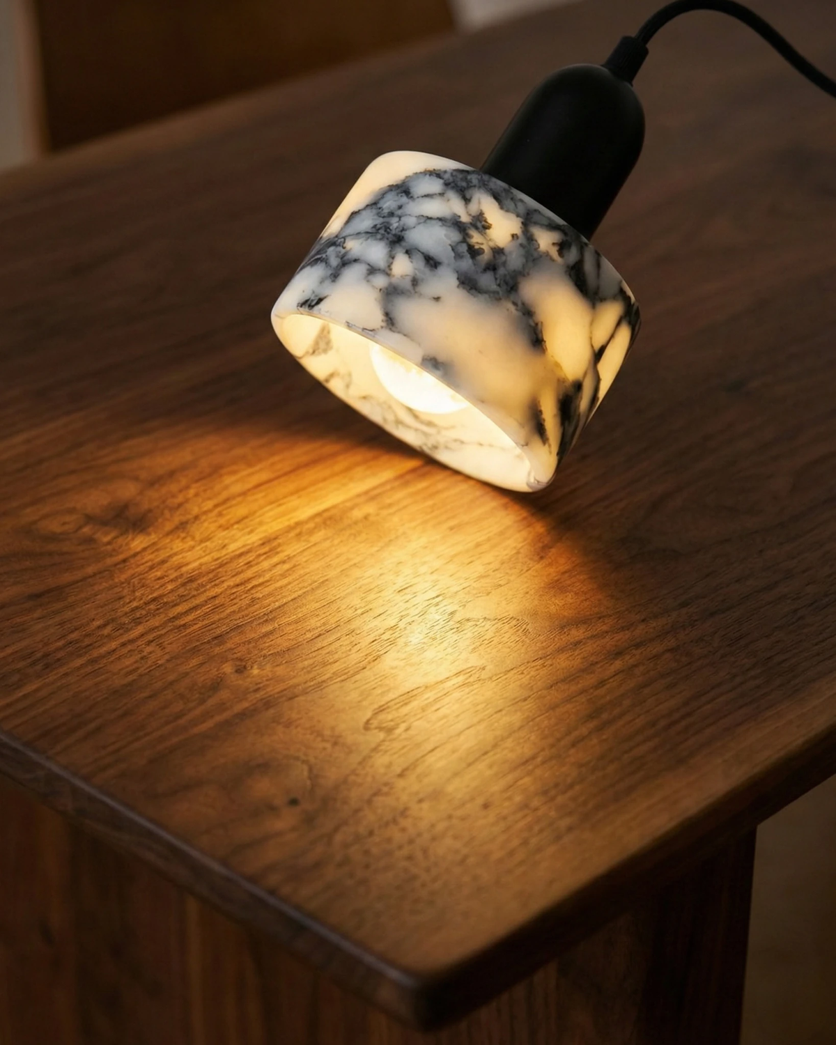 Close-up of the marble pendant light MARMI No.02 hanging lit at an angle over a walnut tabletop
