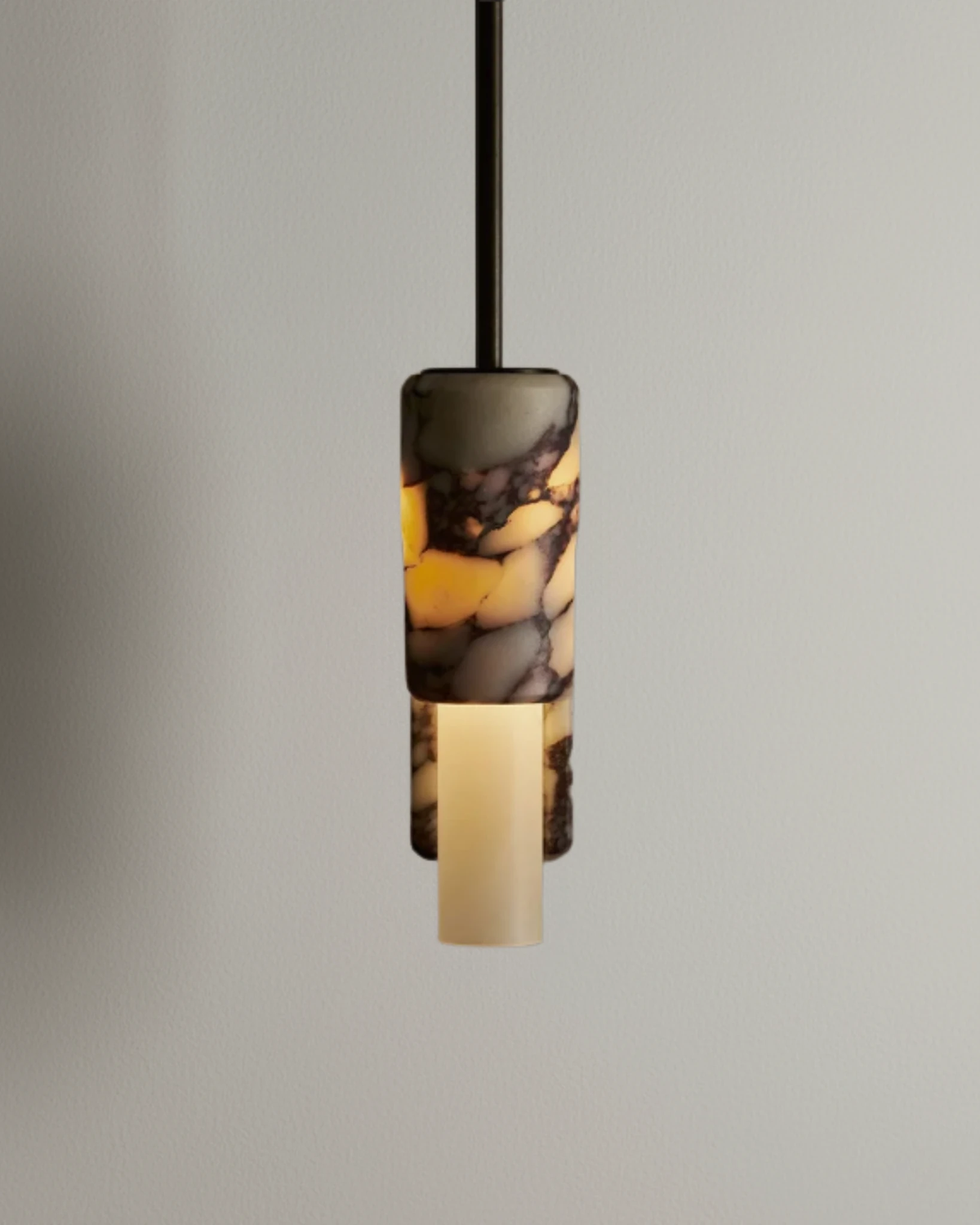 Marble pendant light PALERMO No.01 on a black rod, dark veined marble glowing amber with an ivory lower tube, lit