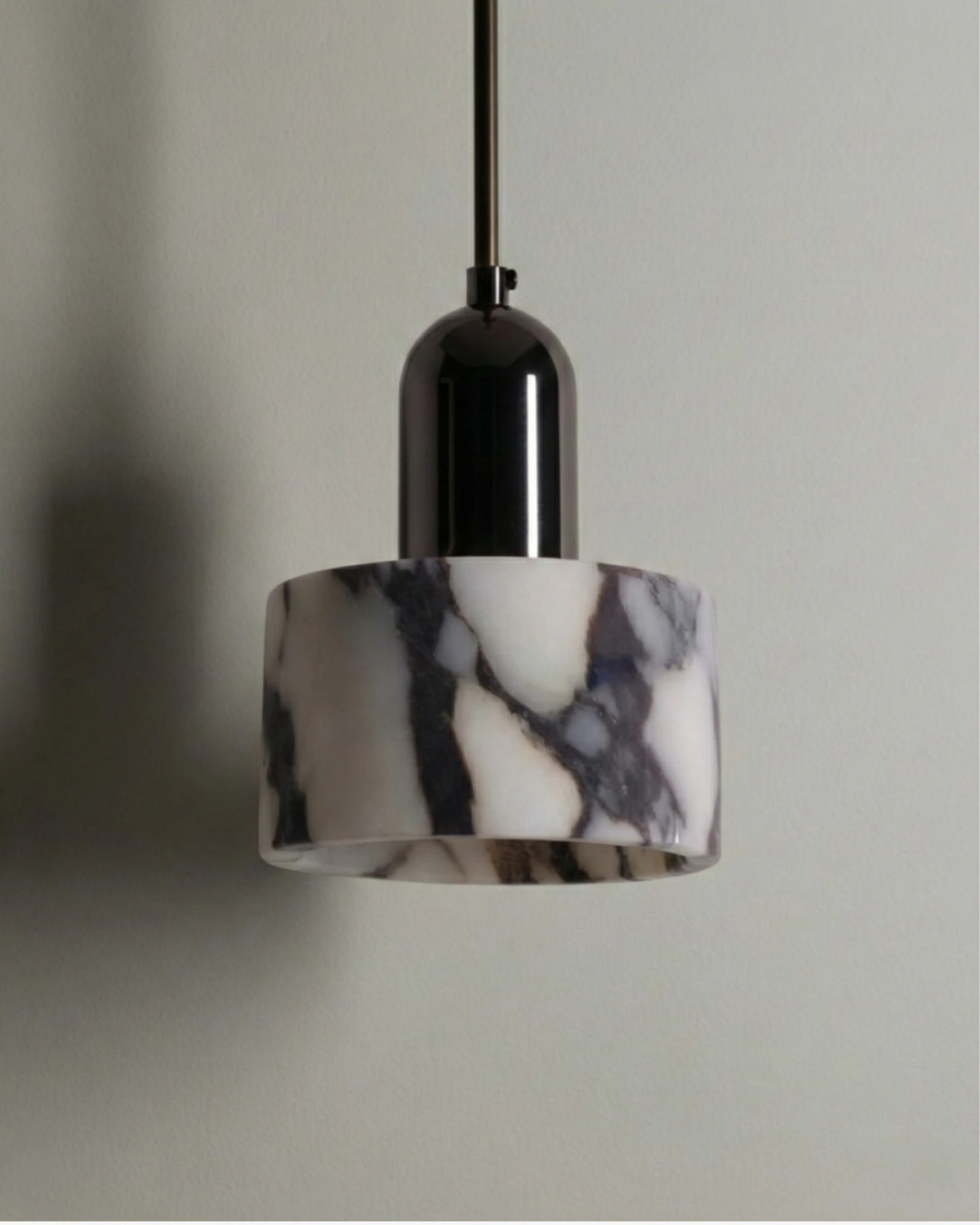 Marble pendant light MARMI No.02 unlit against a gray wall, white marble cylinder with dark veins and a black cap