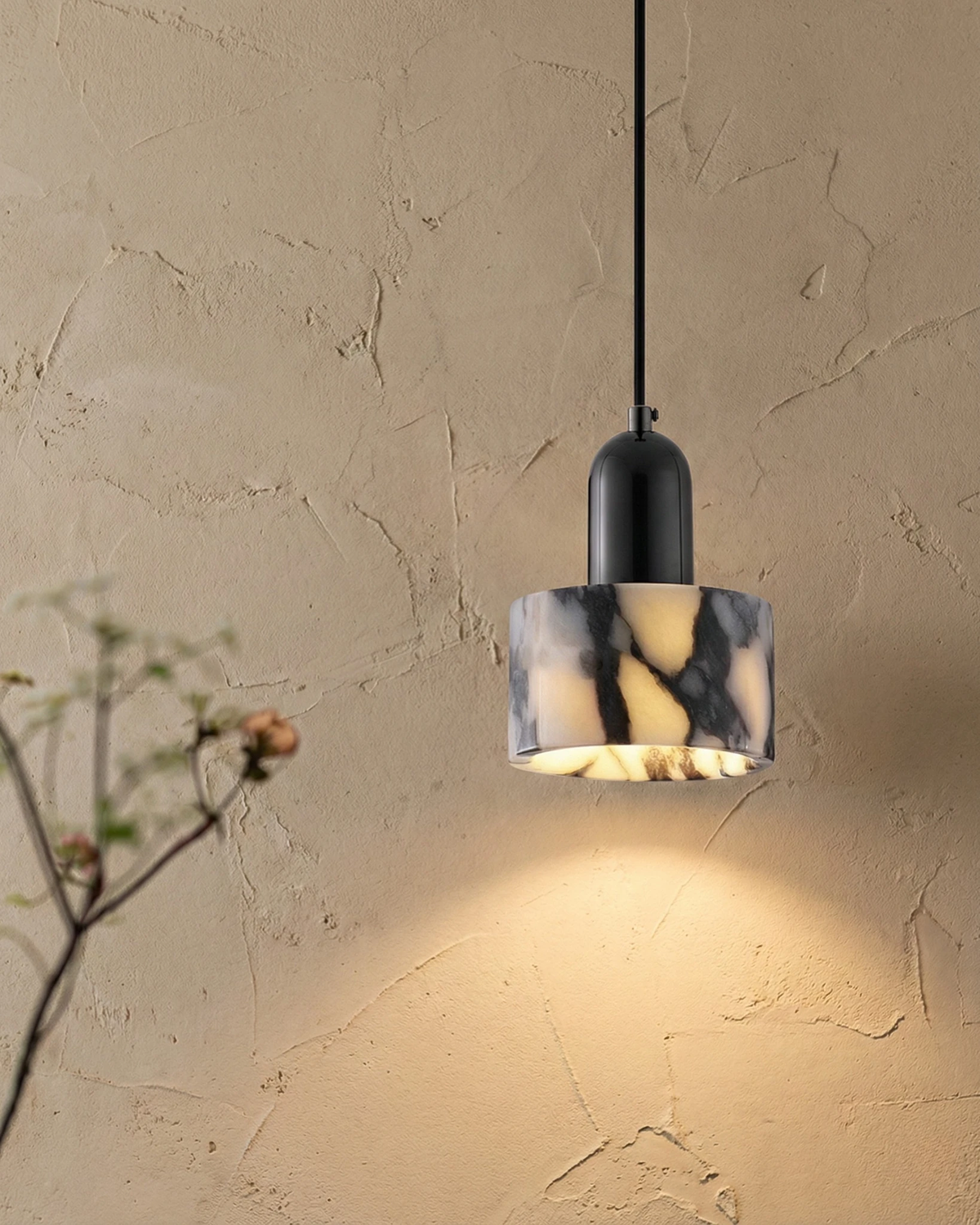 Marble pendant light MARMI No.02 lit against a textured plaster wall beside a bare branch