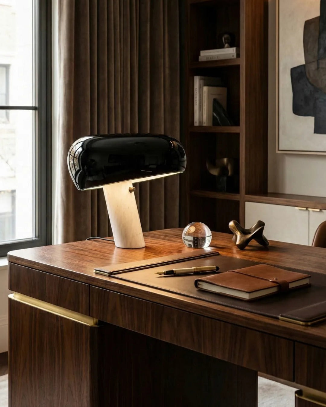 Marble table lamp BRUNO No.01 in black on a walnut desk with a leather notebook, glass paperweight and shelving behind