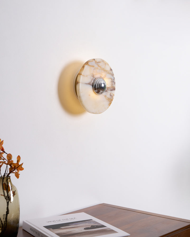 Marble wall sconce LATTE No.01 in chrome switched on above a wooden desk with a vase of orange blossoms
