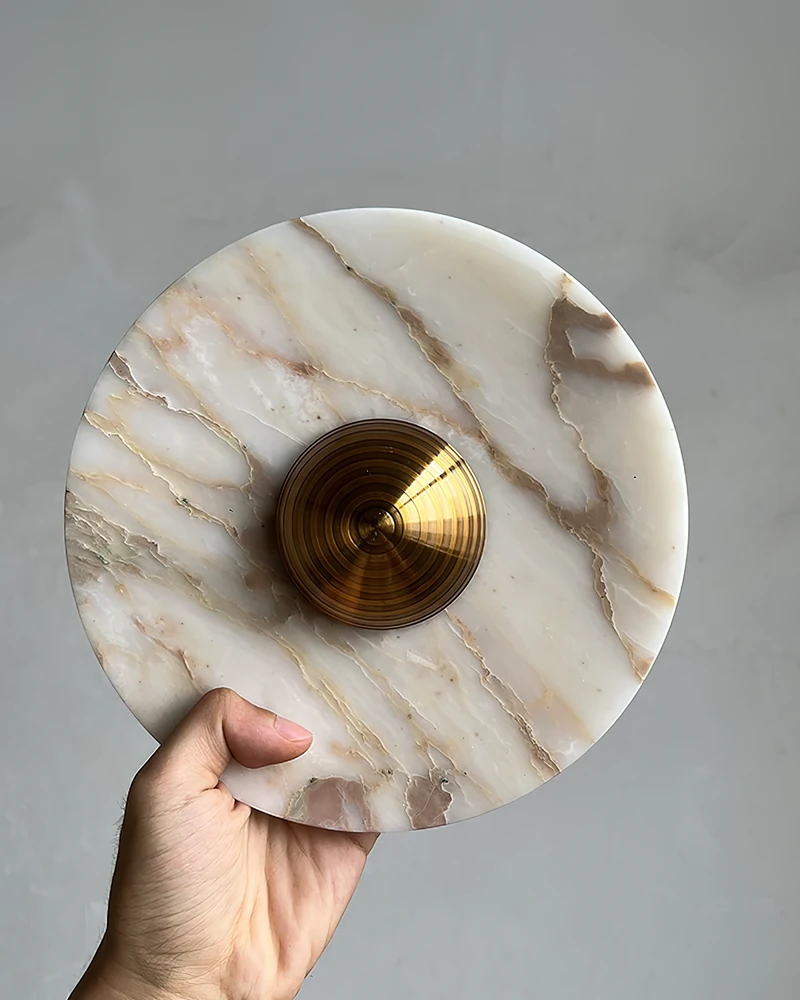 Close-up of a hand holding the LATTE No.01 marble wall sconce disc with a brushed brass center
