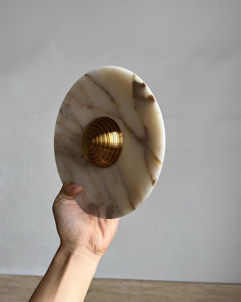 Hand holding the LATTE No.01 marble wall sconce at an angle, gold-veined disc with a ribbed brass dome