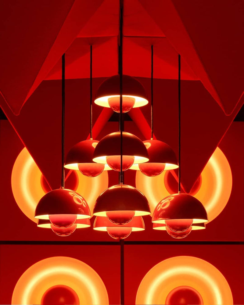 Modern chandelier FLORA No.01 switched on, glowing petal globes against angular red panels in a dramatic red-lit space