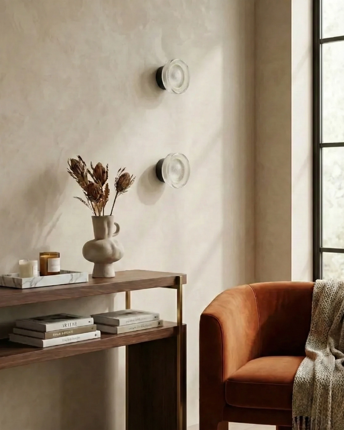 Two modern wall sconces OBLI No.01 stacked on a plaster wall above a walnut console and an orange velvet armchair
