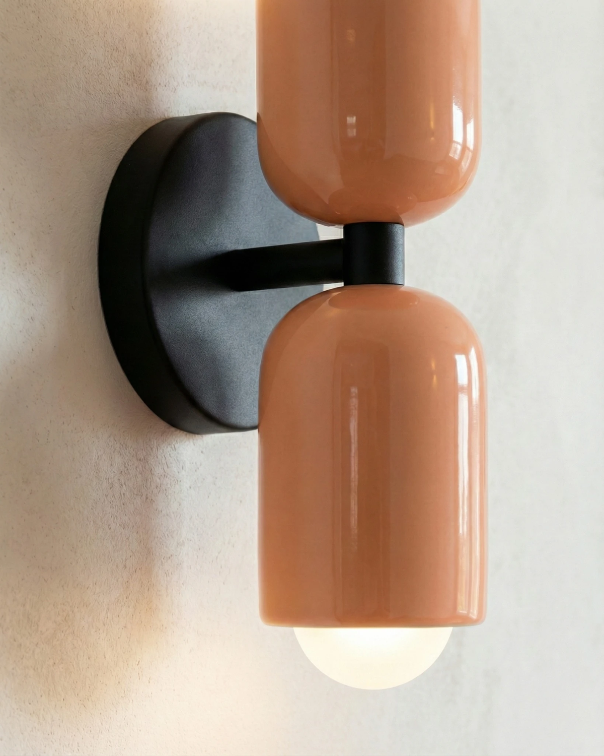 Close-up side view of the TORINO No.01 modern wall sconce in salmon pink on a black bracket, lower bulb lit