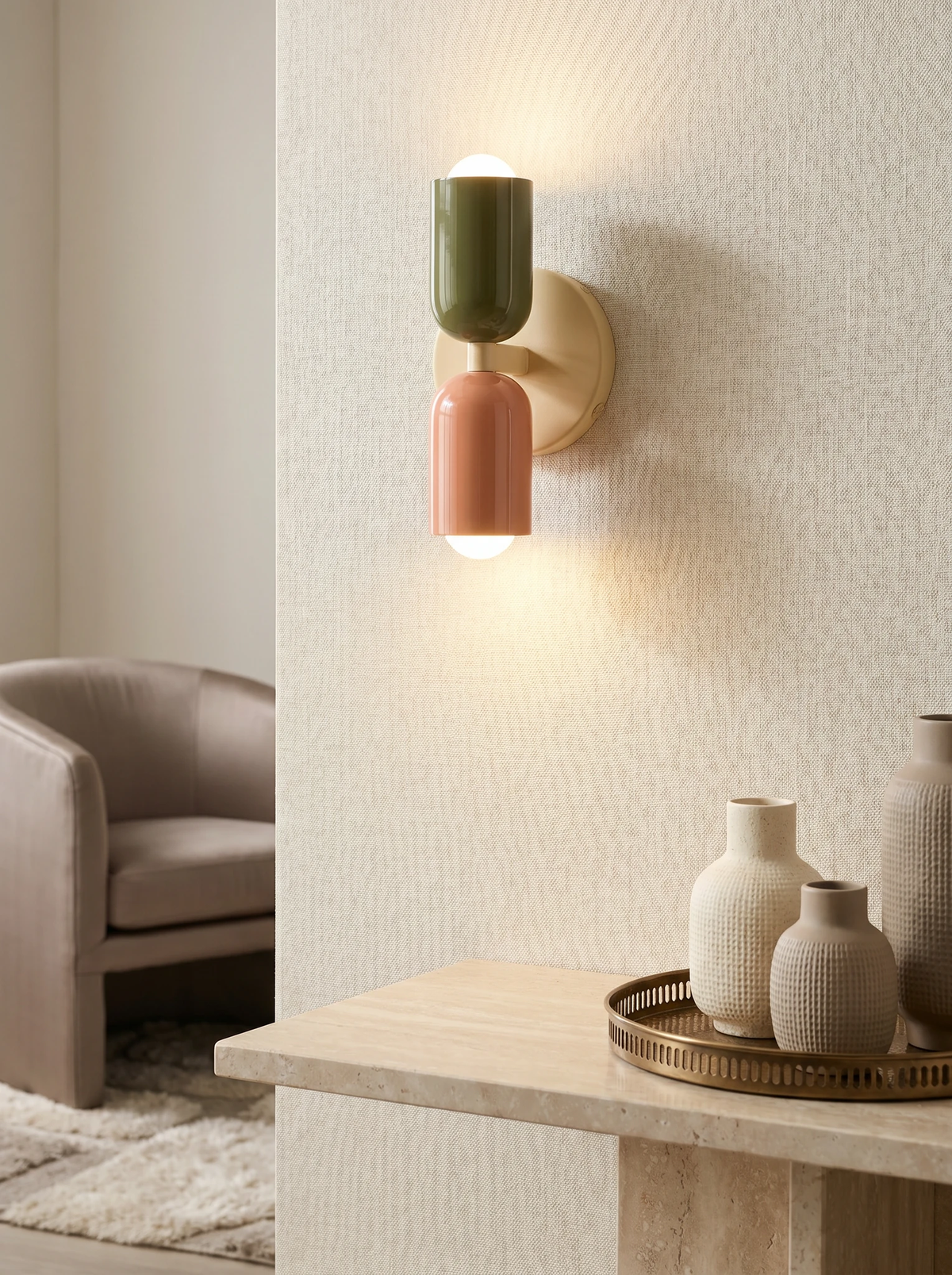 Modern wall sconce MURO No.02, sage and pink capsules lit on a textured plaster wall above a stone ledge with vases