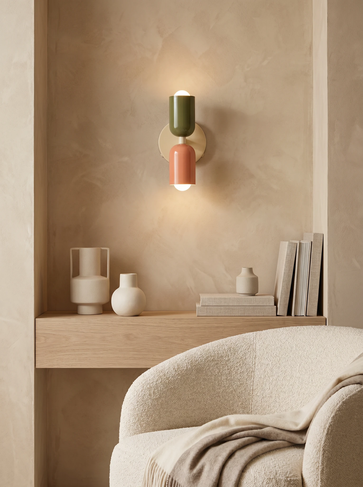 Modern wall sconce MURO No.02 in sage and pink lit inside a plaster niche above a shelf, boucle armchair below