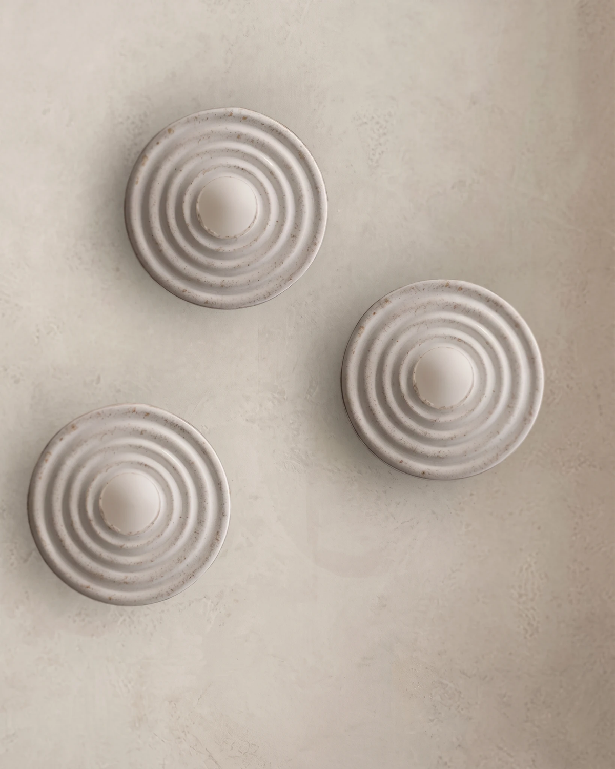 Three modern wall sconces ANIMA No.01 in antique white, rippled resin discs unlit on a plaster wall