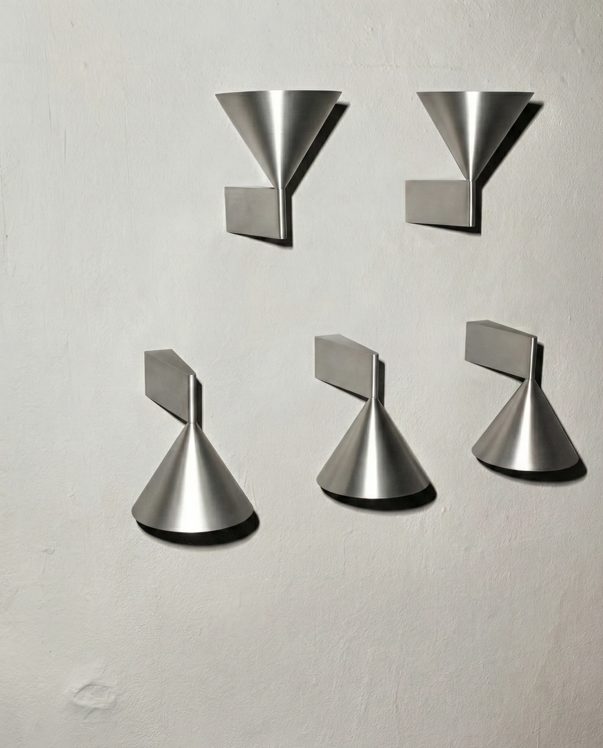 Five modern wall sconces ETNA No.01 in brushed aluminum arranged in two rows on a plain wall, unlit