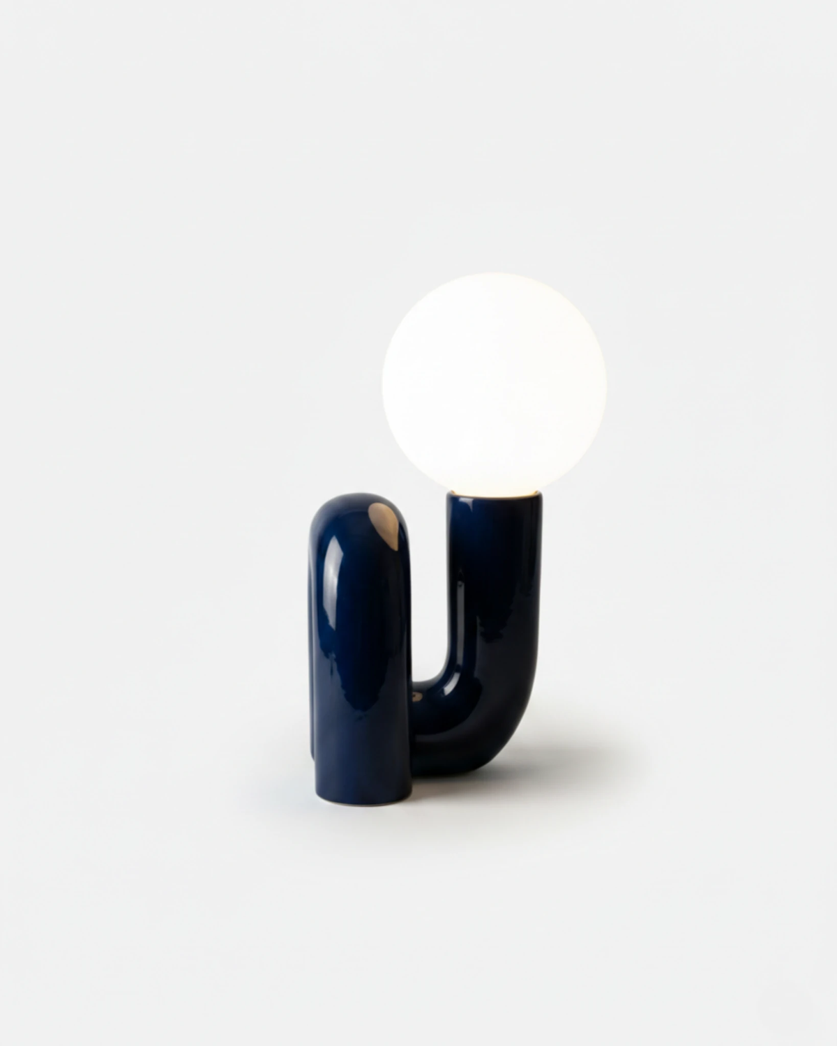 Opal globe table lamp VICO No.01 in French Blue, sculpted U-shaped resin base, globe lit on a white background