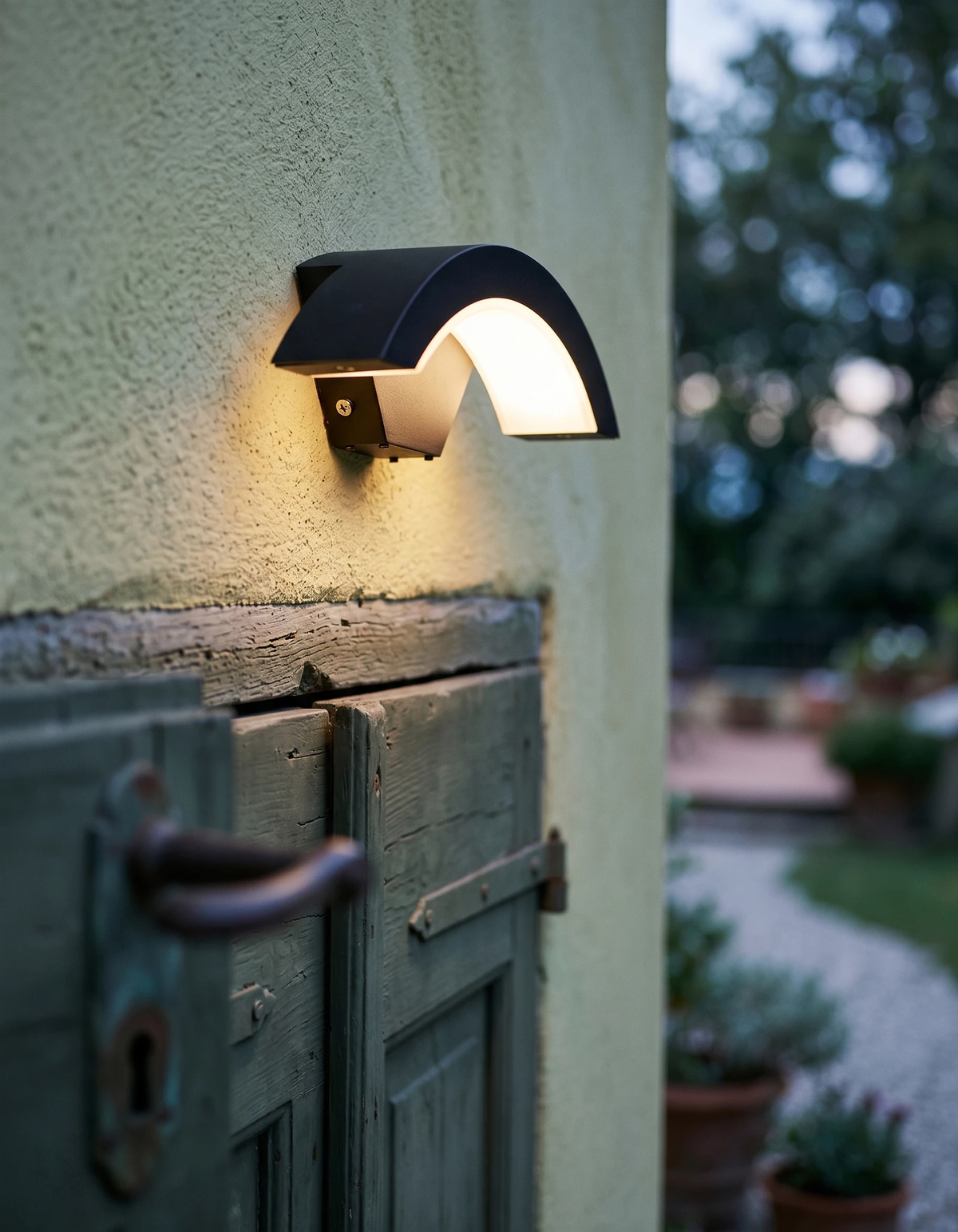 Outdoor wall sconce BALCONE No.01 switched on above a weathered green wooden door at twilight