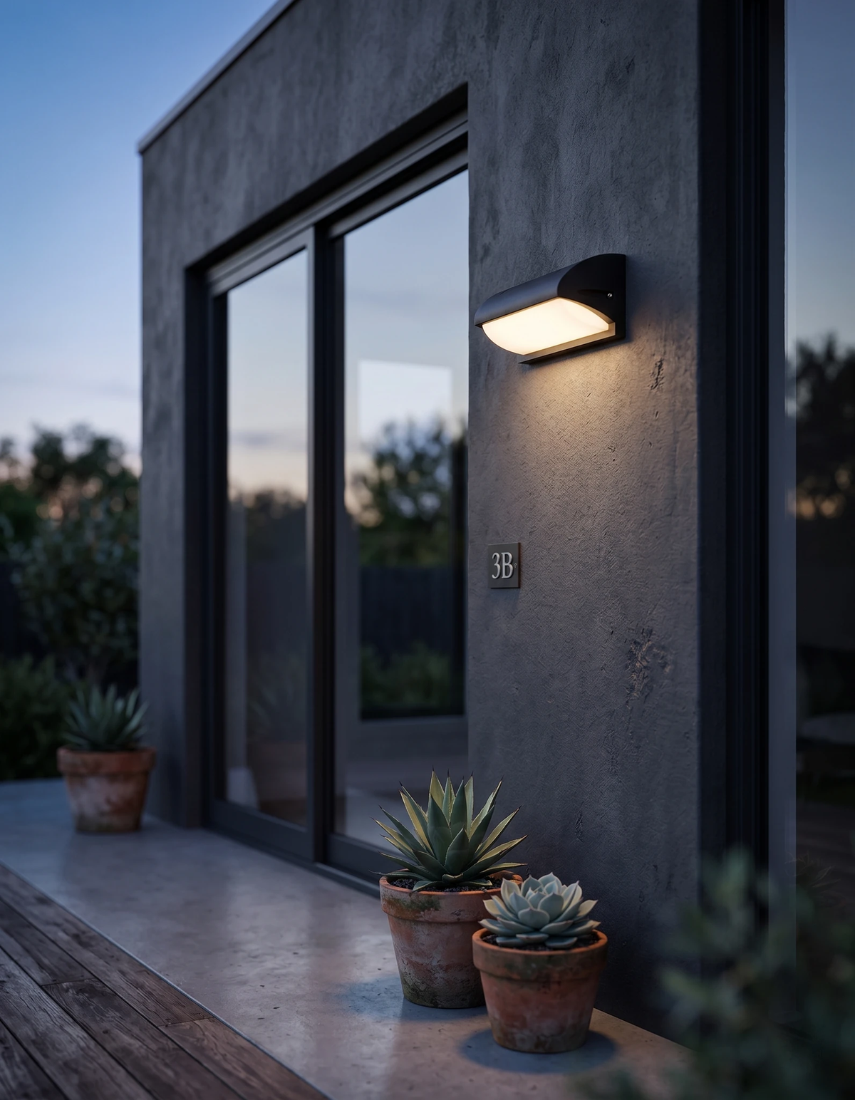 Outdoor wall sconce NOTO No.04 glowing beside a sliding glass door on a charcoal facade with potted succulents