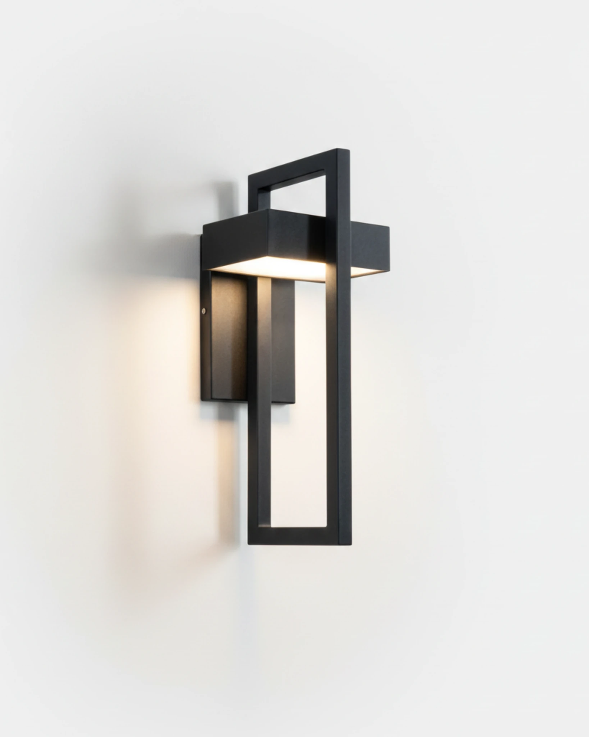 Outdoor wall sconce FERRO No.01 in the wide size, black open-frame lantern with downlight switched on, white wall