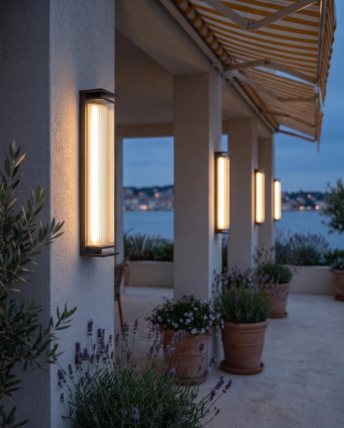 Outdoor wall sconce COSTA No.01, a row of lit columns along a covered terrace with striped awnings by the sea