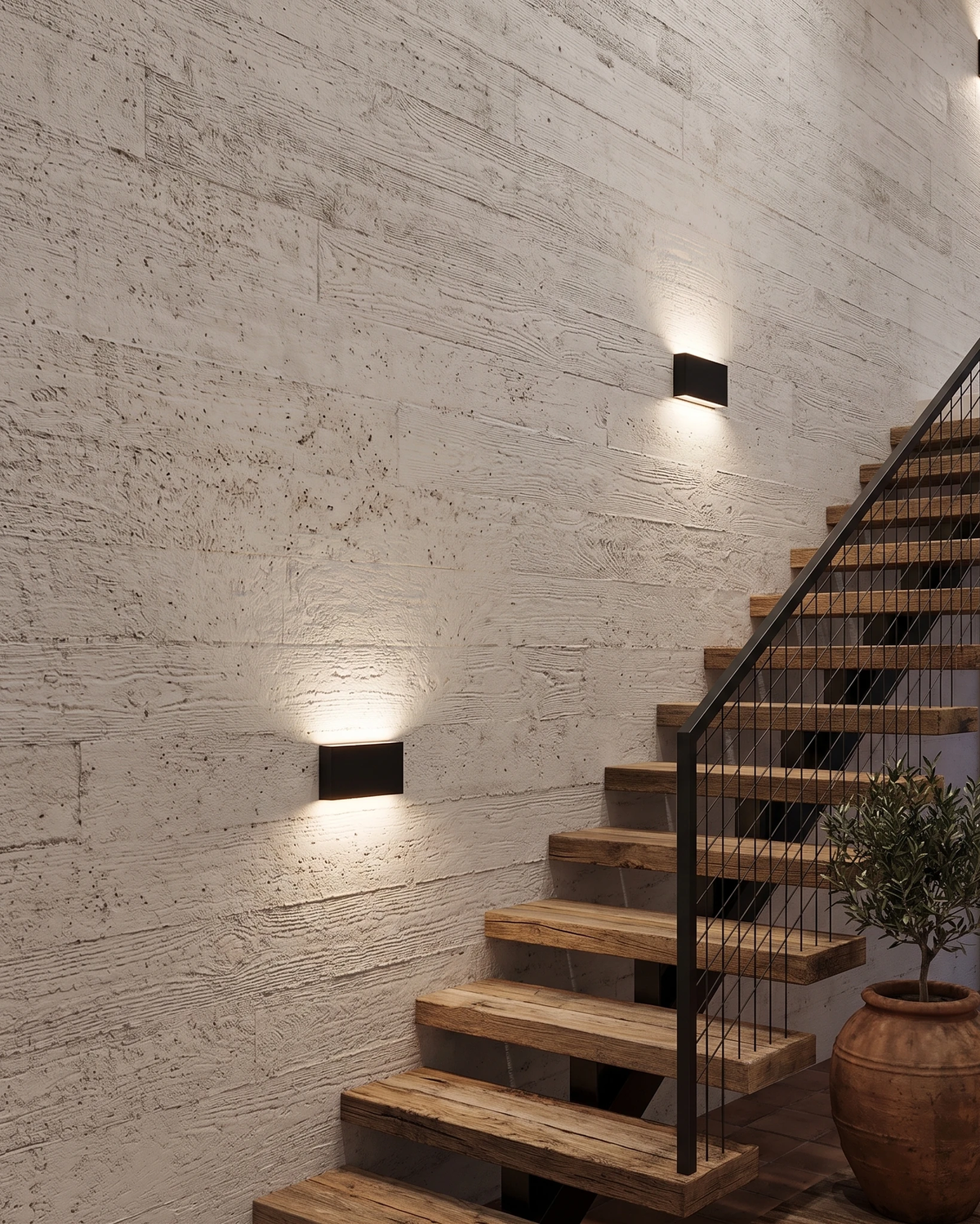 Two outdoor wall sconces PISA No.01 in deep black lit on a limestone wall beside a wooden staircase