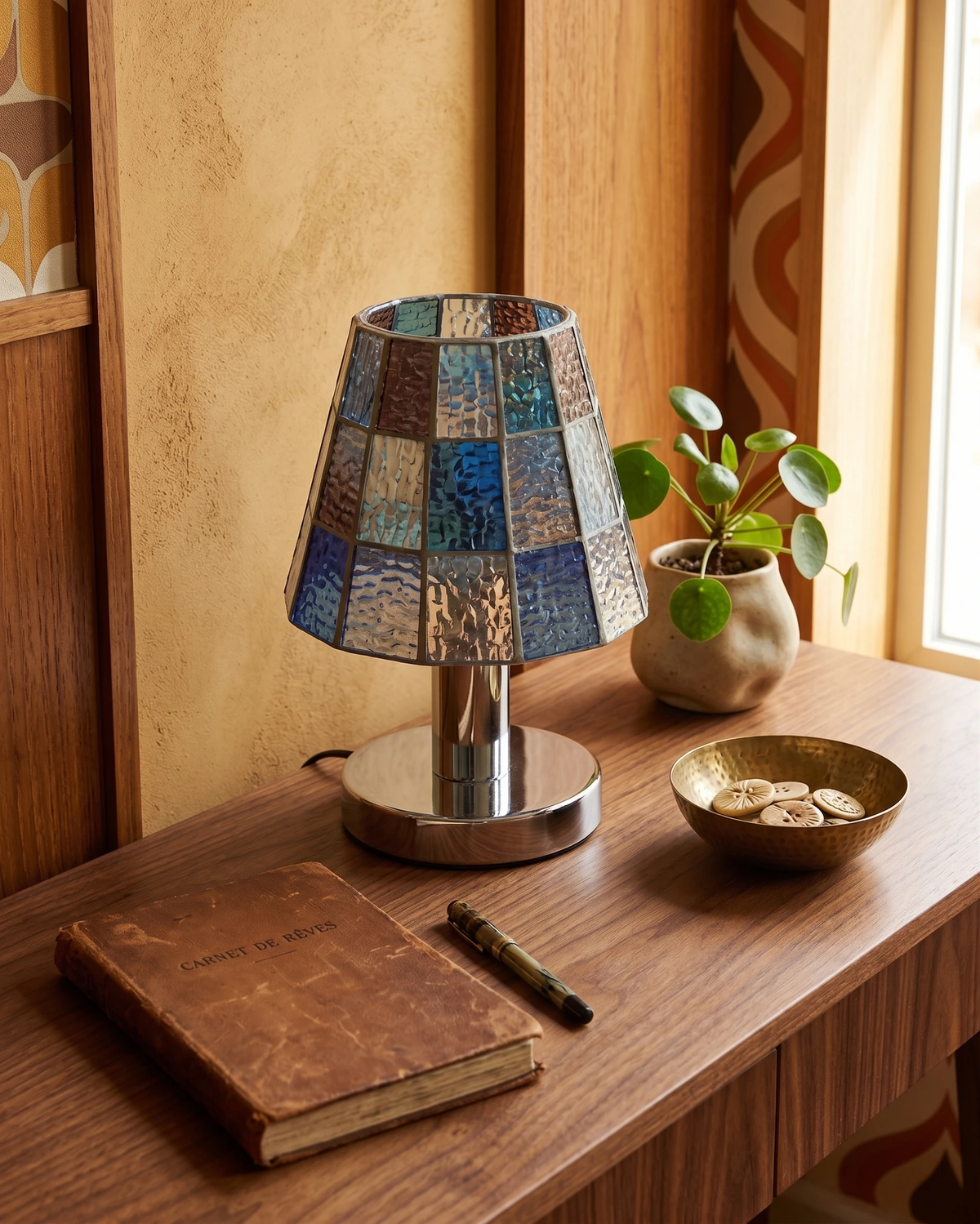 Stained glass table lamp VETRA No.01 in cobalt blue, lit on a wooden desk with a leather journal and a bowl