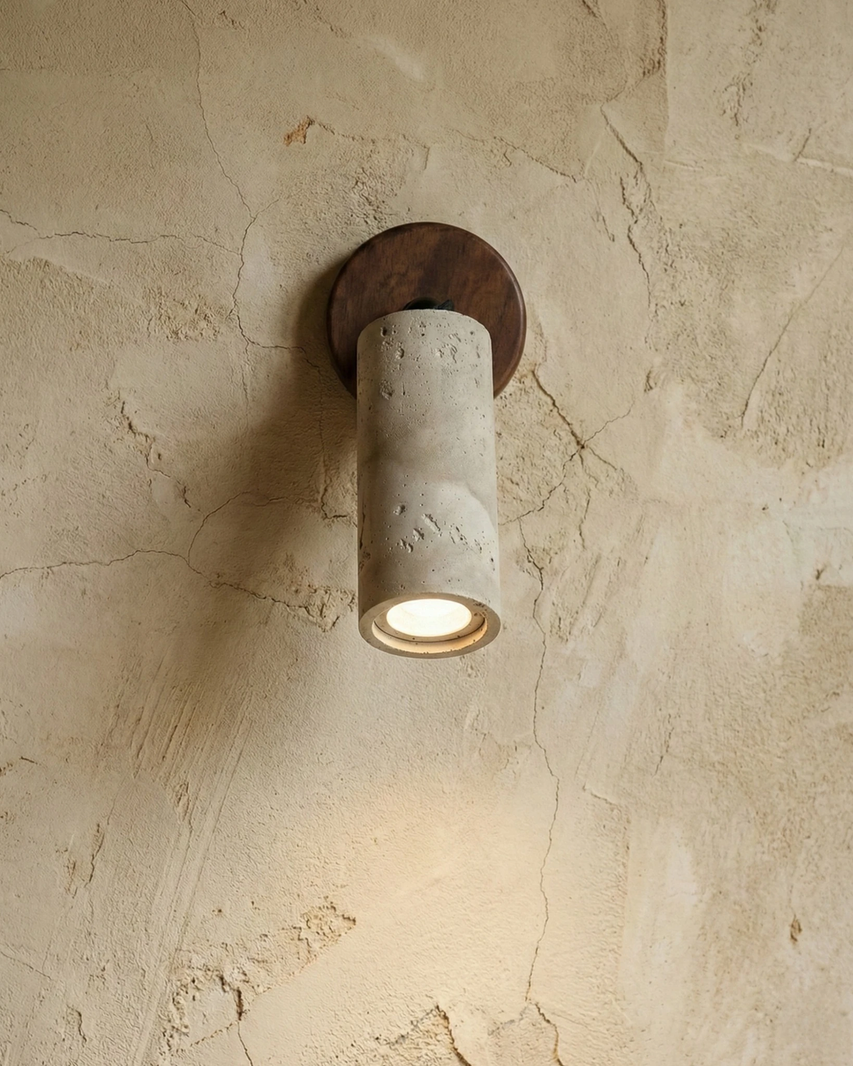 Close-up of the MANTOVA No.01 stone-effect wall sconce, stone-effect cylinder on a walnut disc casting a spot down a plaster wall