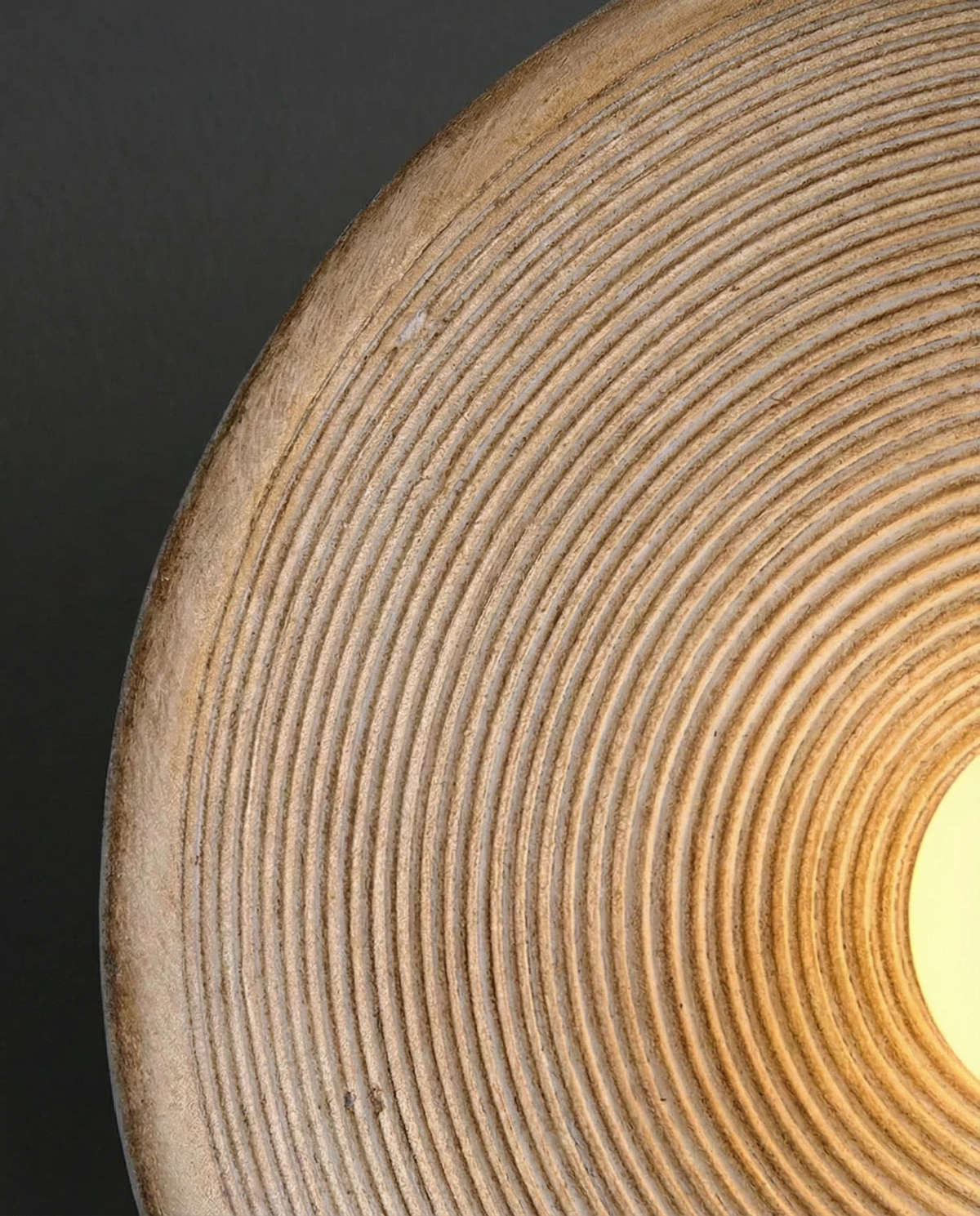 Close-up of the concentric ridges of the ECCO No.01 stone-look wall sconce with the pearl bulb glowing