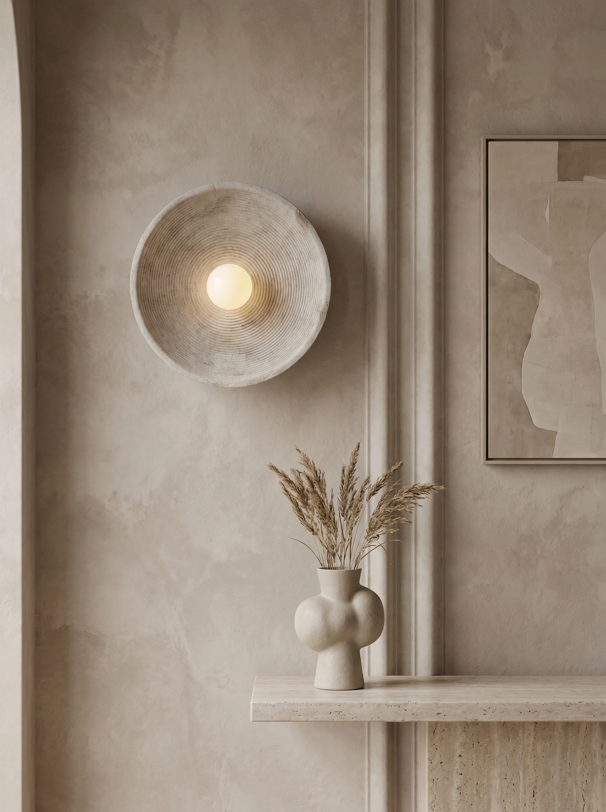 Stone-look wall sconce ECCO No.01 in warm cream, switched on above a stone ledge with a vase of dried grass
